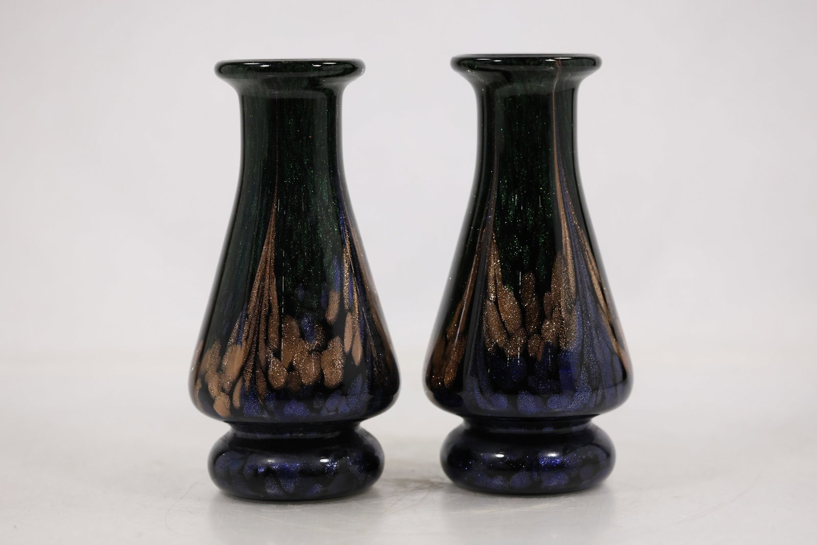 Pair Black Iridescent Art Glass Bud Vases: A pair of slender black art glass bud vases has narrow necks rounded bases and iridescent surface color. Their matched form and reflective finish are visible from multiple angles and no maker is confi