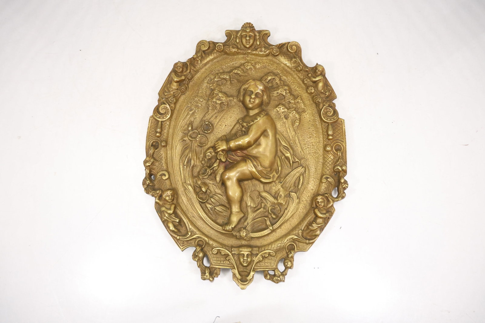 Ornate Brass Religious Figural Wall Plaque: An ornate brass wall plaque carries a raised religious figure within an architectural decorative frame. The cast relief metal surface and hanging format are visible in the photographs and no maker is