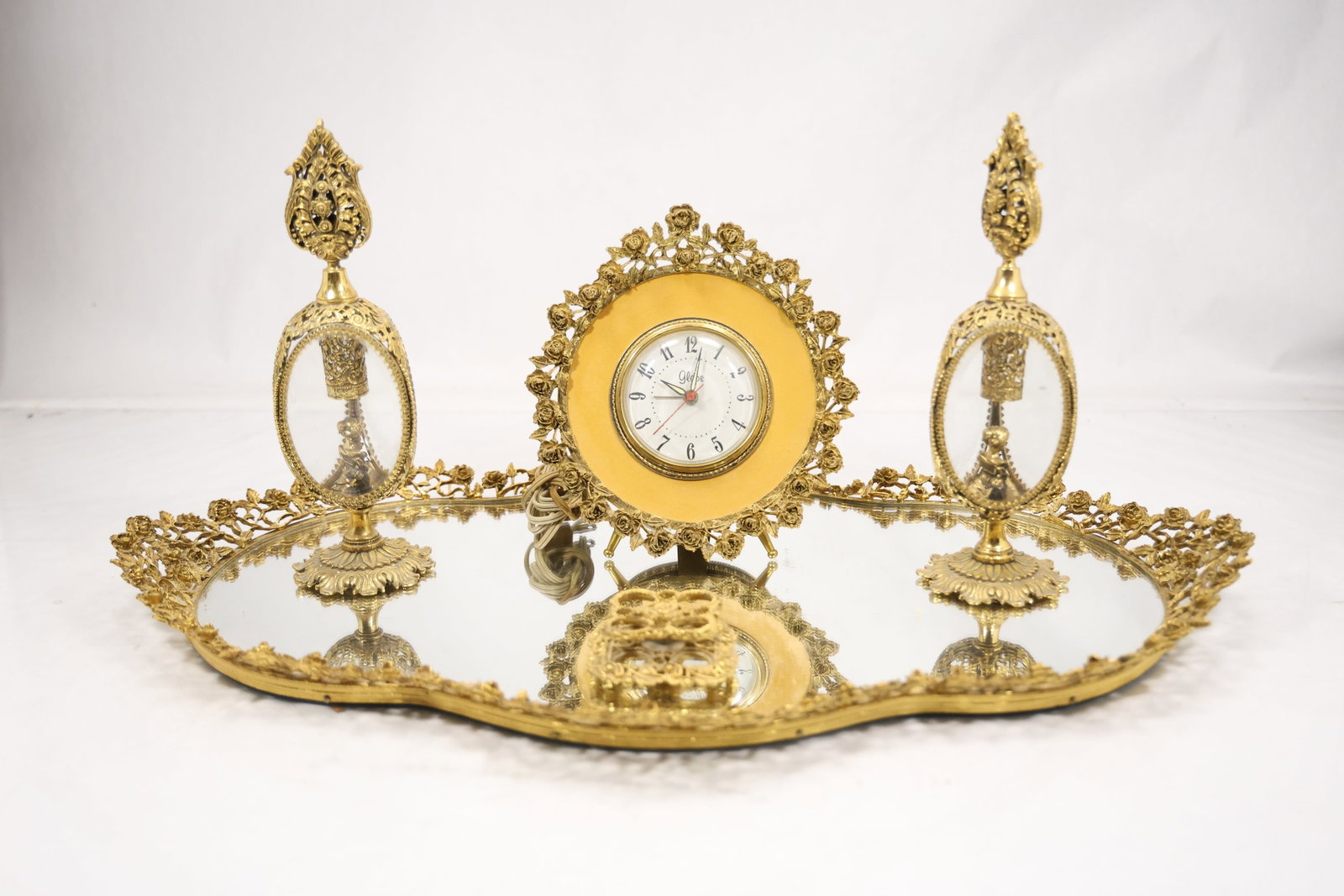 Brass Mirrored Vanity Tray with Four Accessories: A brass tone vanity set includes a mirrored tray and four coordinated dressing table accessories. The matching metal frames reflective base and small container forms identify the group as a vanity ens