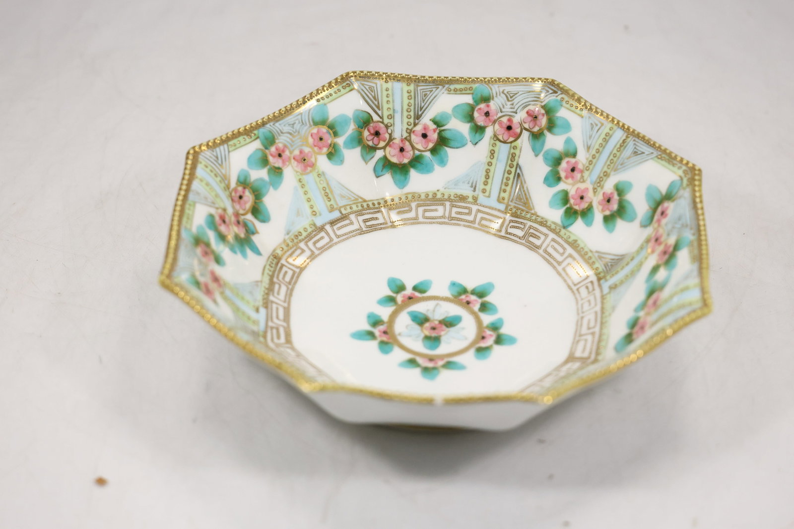 Floral Decorated Porcelain Octagonal Bowl: A porcelain bowl has an octagonal rim and multicolor floral decoration over a light glazed ground. The angular serving form and botanical pattern are visible in the photographs and no maker is confirm