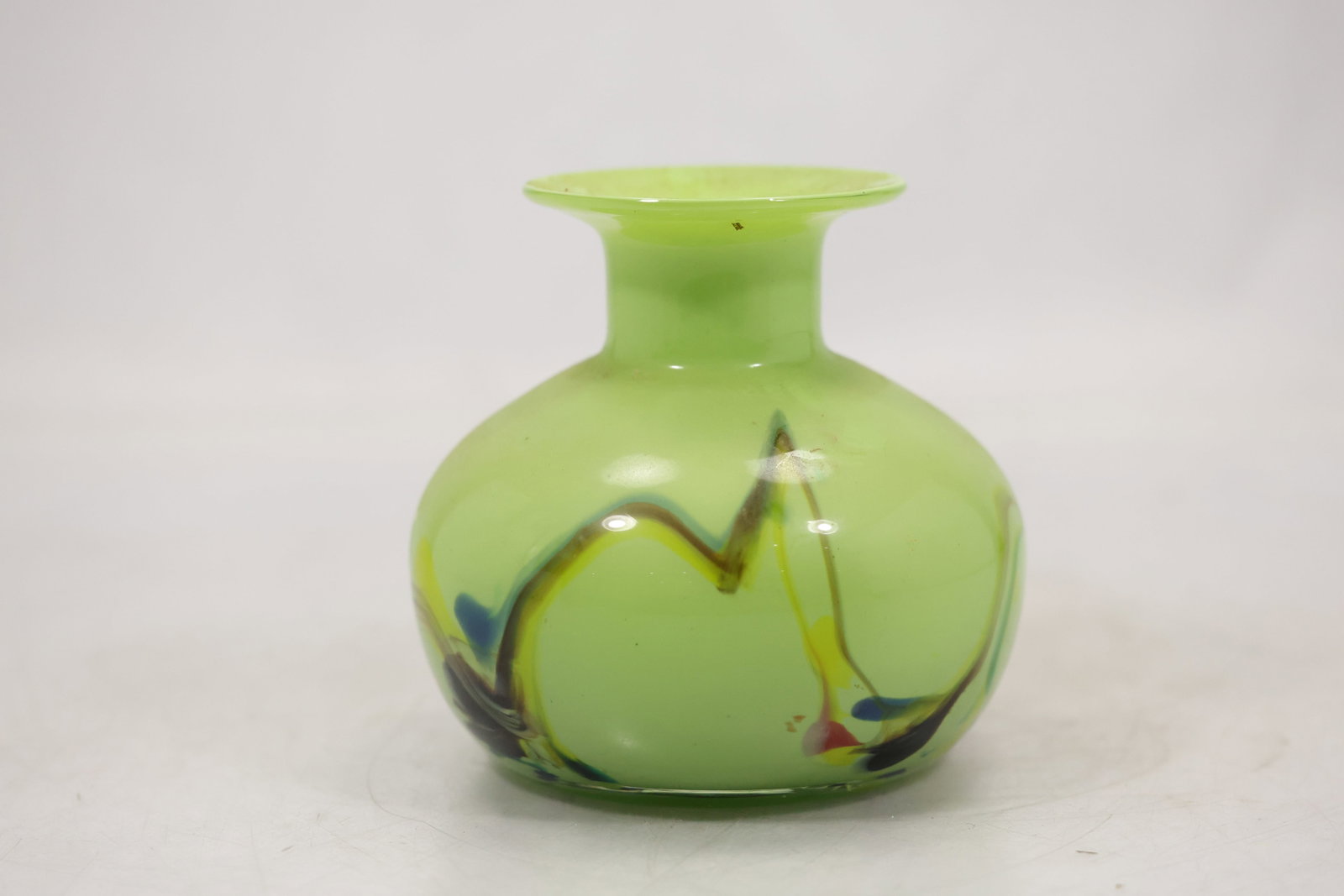 Lime Green Art Glass Vase with Black Applied Trail: A lime green art glass vase has a rounded body and contrasting black applied glass trail around the exterior. The vivid color combination and raised decoration create a modern sculptural vessel and