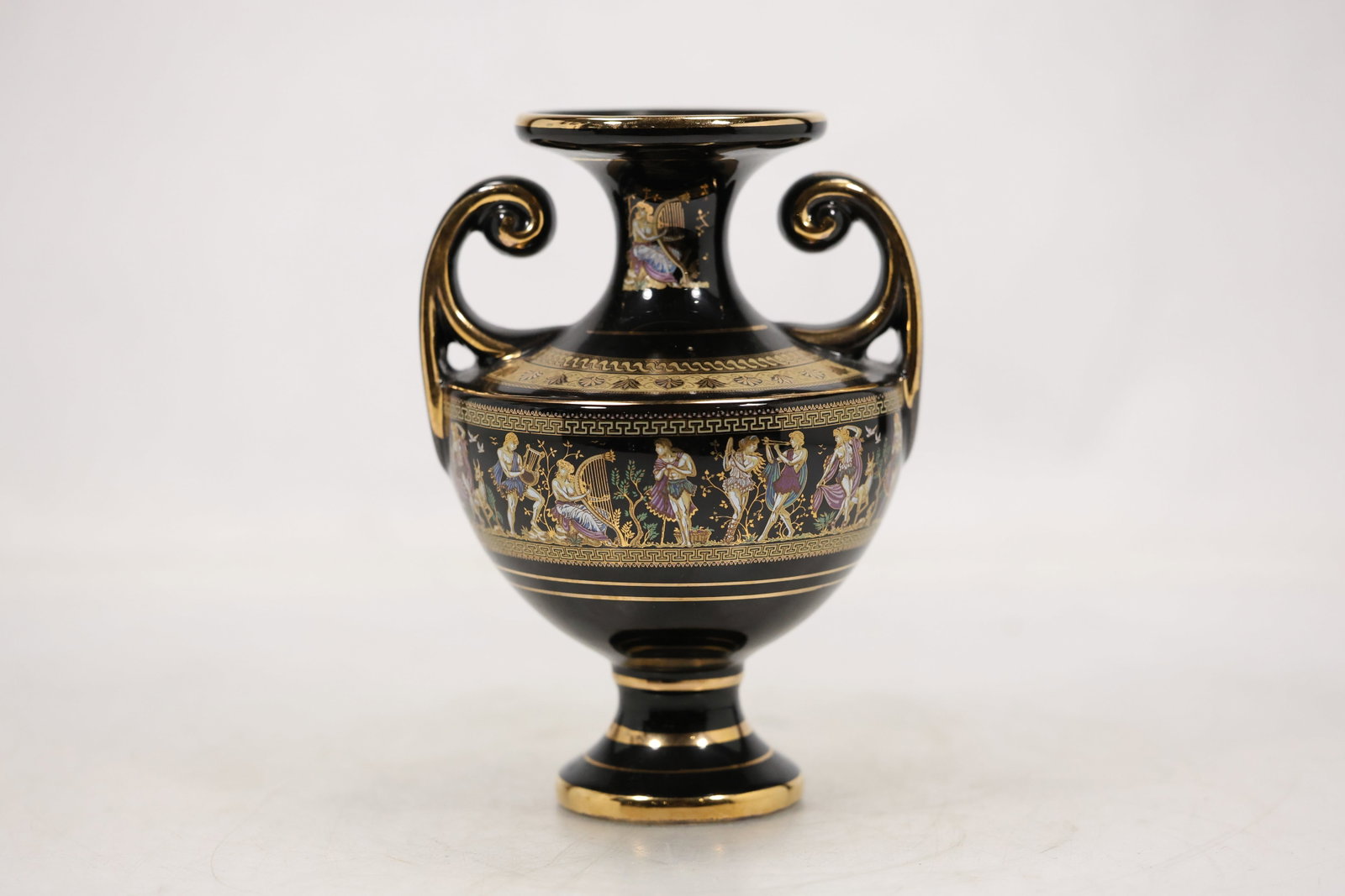 Black and Gold Classical Double Handle Urn: A decorative urn has a black body with gold tone classical ornament paired handles and a flared foot. The symmetrical amphora form and contrasting surface decoration are visible in the photographs and