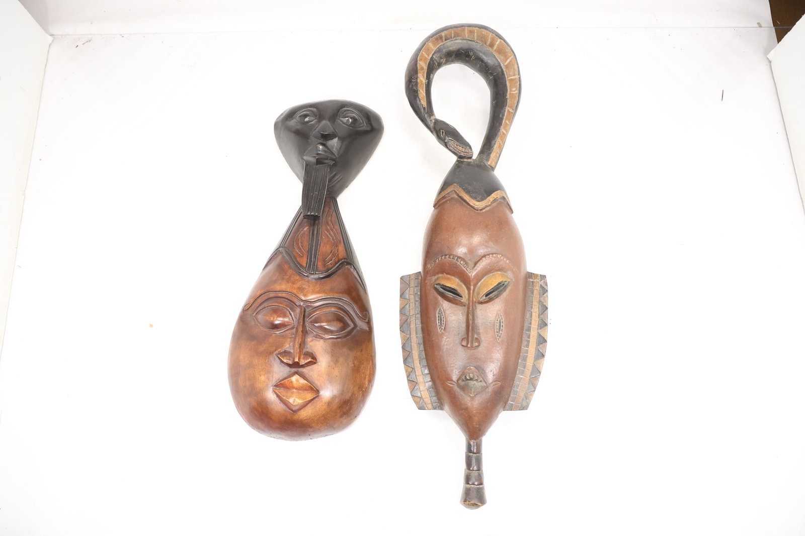 Pair Carved Abstract Wood Figural Masks: A pair of carved wood masks has elongated abstract faces with incised features and darkened accents. The matched wall display format and hand worked surfaces are visible in the photographs and no