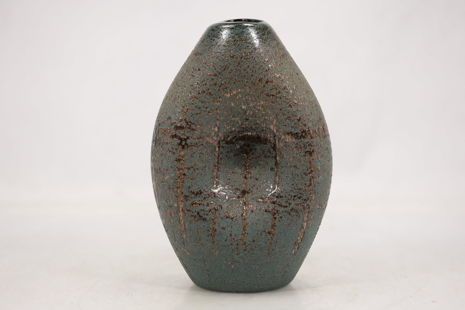 Metallic Glaze Modernist Pottery Vase: A modernist pottery vase has a compact sculptural body with a metallic glaze and narrow opening. The reflective surface irregular profile and hand formed appearance support a studio pottery