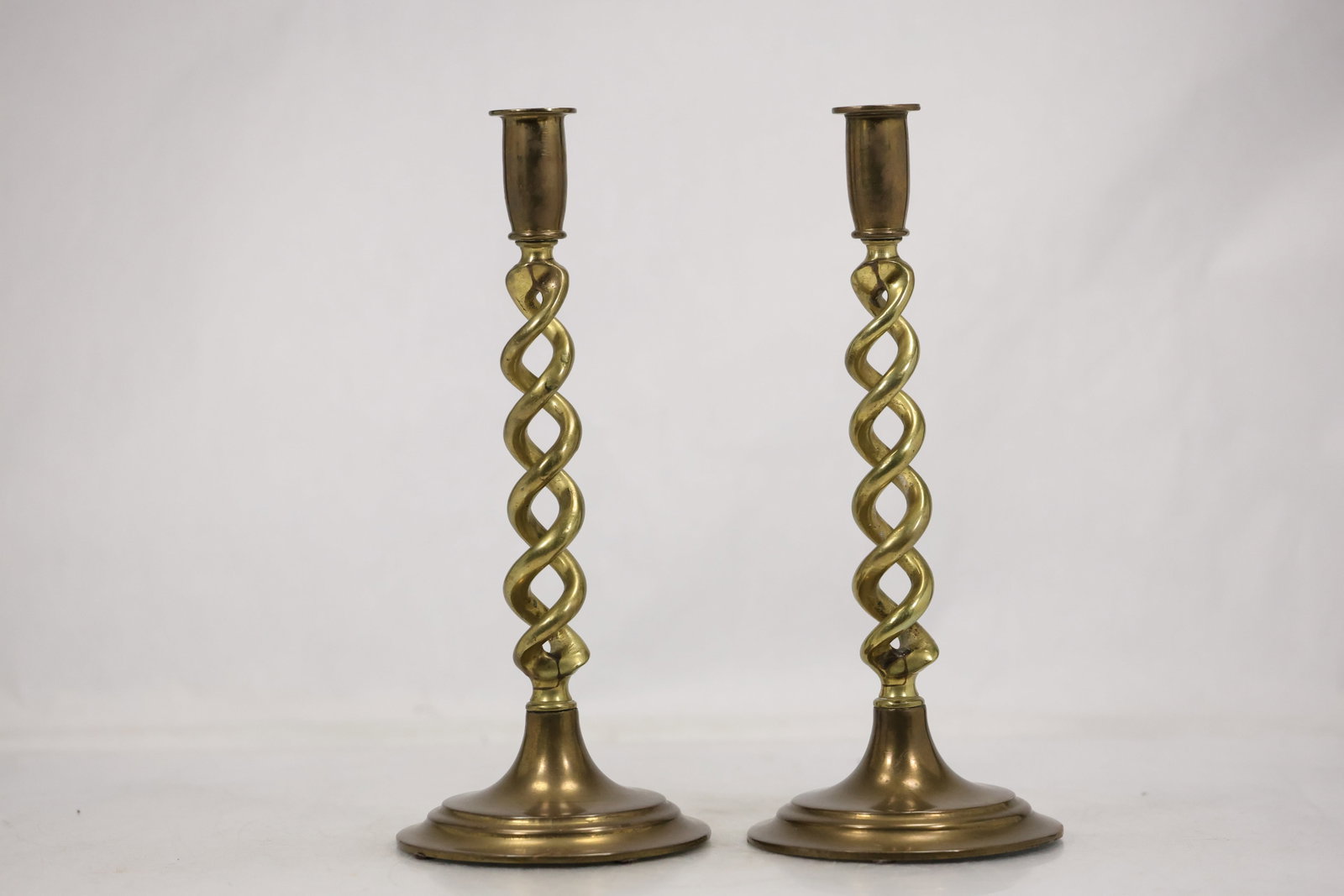 Pair Brass Spiral Stem Candlesticks: A matched pair of brass candlesticks has circular bases spiral twisted stems and single candle sockets. Their repeated form and polished metal surface identify them as a coordinated table pair and no