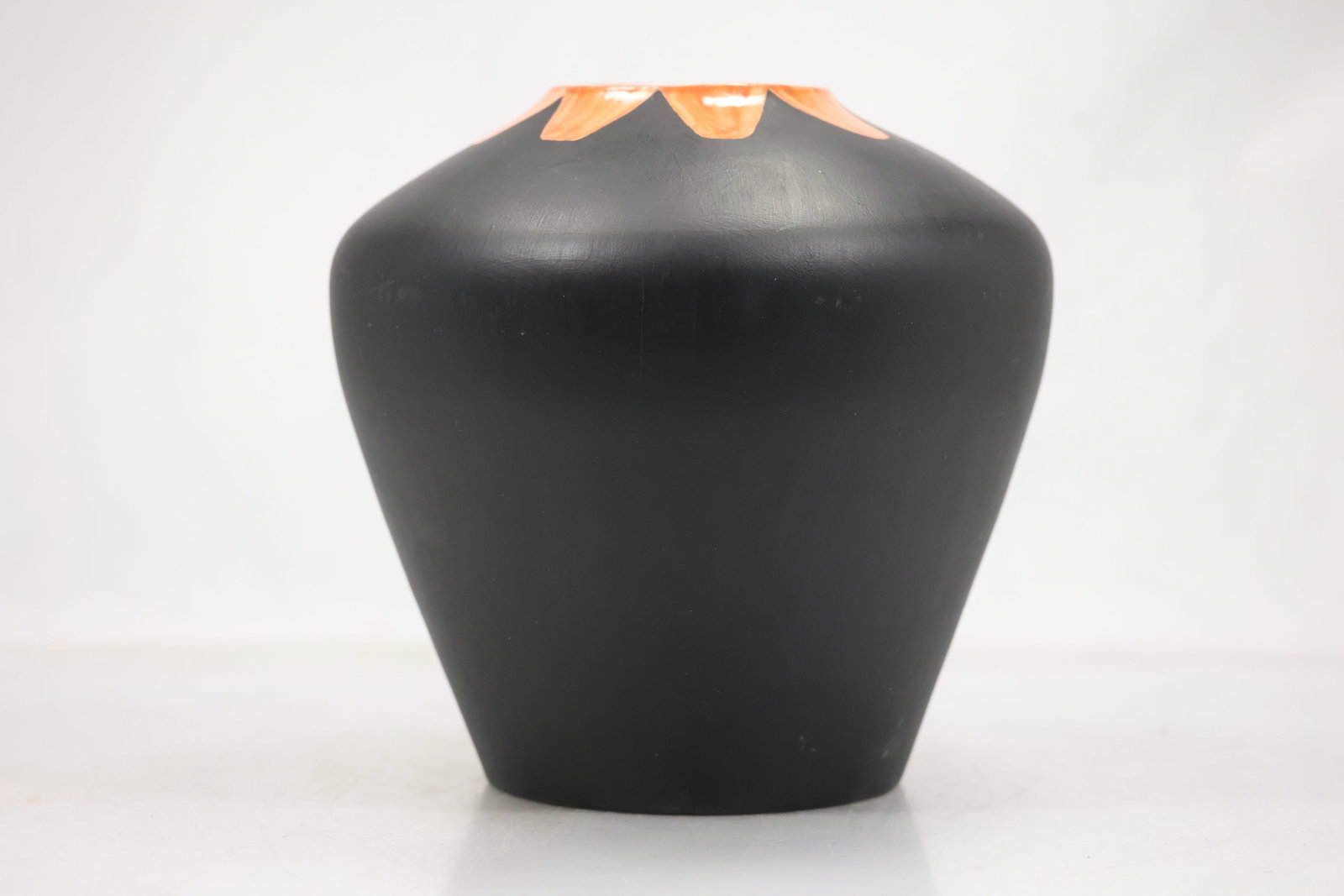 Black Pottery Vase with Orange Drip Rim: A pottery vase has a black glazed body with a bright orange rim and downward drip decoration. The bold color contrast rounded profile and controlled glaze runs support a studio pottery identification