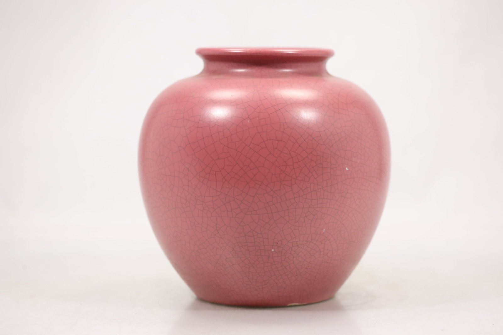 Pink Crackle Glaze Pottery Vase: A pottery vase has a rounded body with pink crackle glaze and a narrow circular mouth. The deliberately crazed surface and uniform color are visible in the photographs and no maker is confirmed. Its