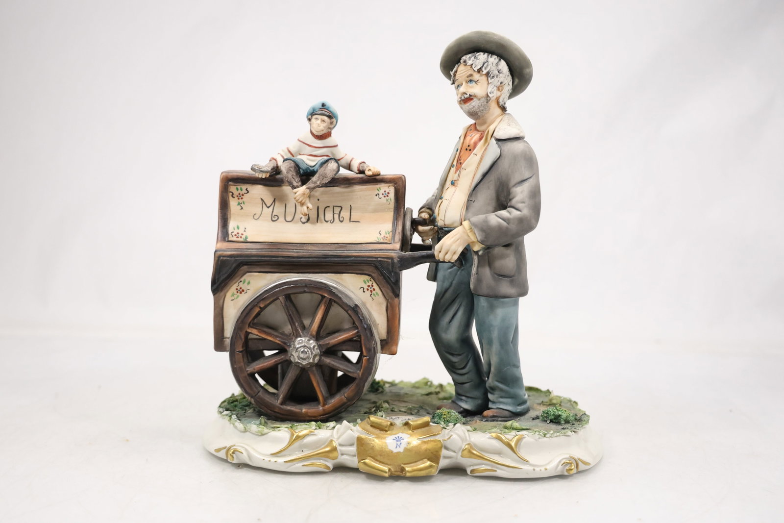 Ceramic Musician with Wheel Figural Sculpture: A glazed ceramic sculpture depicts a musician posed beside or holding a large wheel form element. The modeled human figure musical theme and integral base are visible in the photographs and no artist