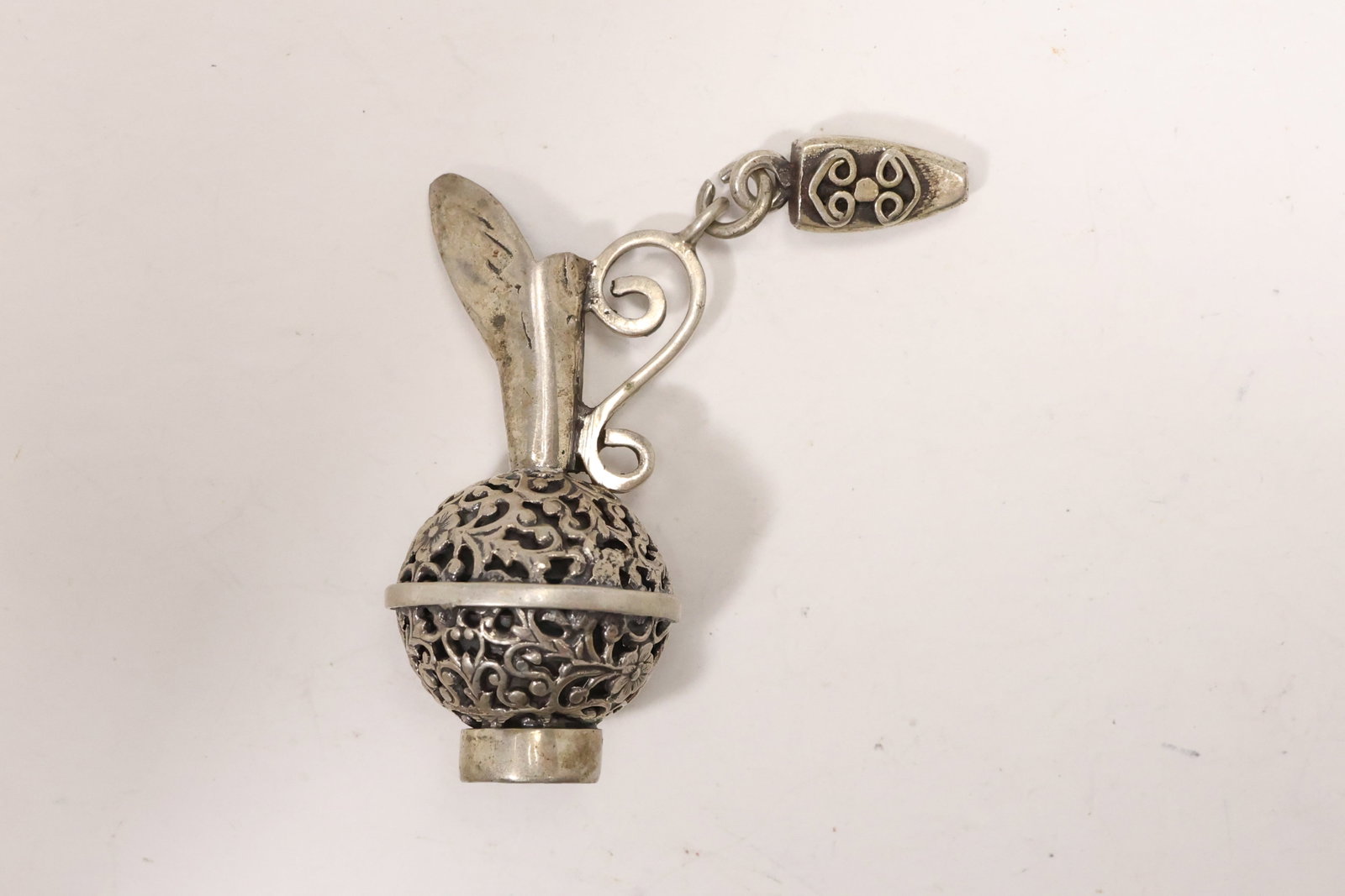 Sterling Silver Ewer Form Bottle Stopper: A sterling silver bottle stopper is modeled as a miniature ewer with an ornate perforated body curved handle and projecting spout. The figural vessel top is attached to a tapered stopper fitting. The 