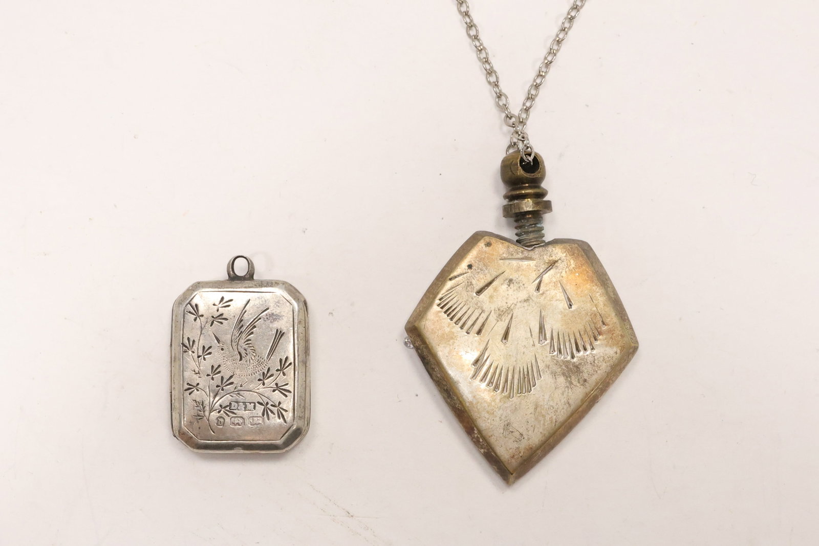 Two Sterling Silver Perfume Bottles and Locket: A sterling silver group includes two miniature perfume or scent bottles and one oval locket. Engraved and relief decoration appears across the small personal accessories. The silverwork relates broadl