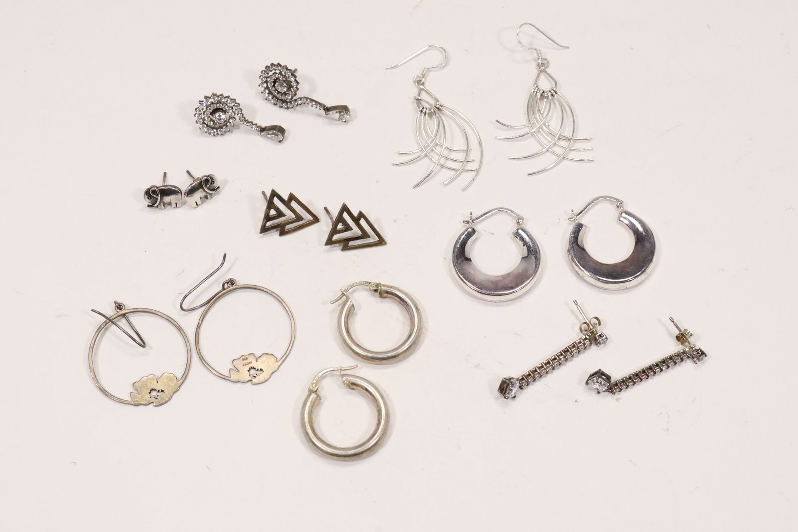 Eight Pairs Sterling Silver Figural and Drop Earrings: A group of eight pairs of sterling silver earrings includes triangular forms long wire drops cutout hoops polished hoops elephants swirls and cubic zirconia accents. The mixed group totals 27 grams ac
