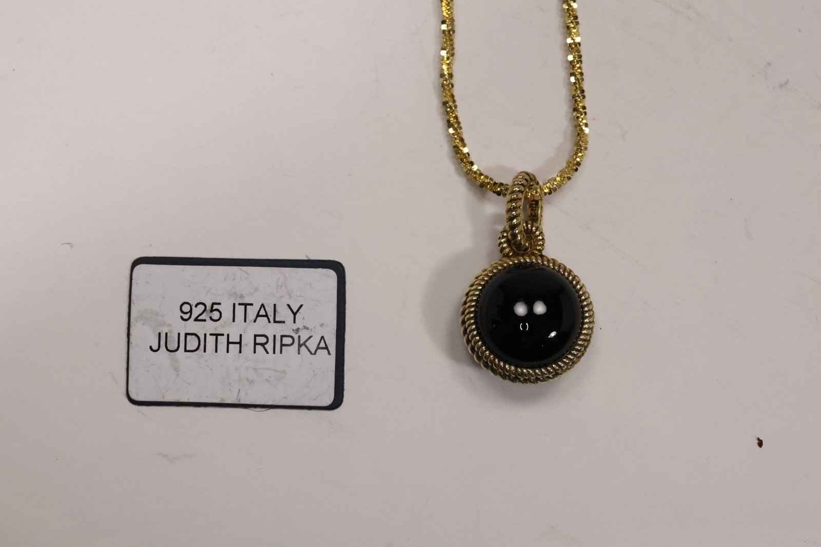 Judith Ripka Sterling Silver Black Onyx Pendant Necklace: A Judith Ripka pendant necklace has a cushion form black onyx center in a textured .925 sterling silver mount suspended from a sterling chain. The maker identification follows the pictured label and d