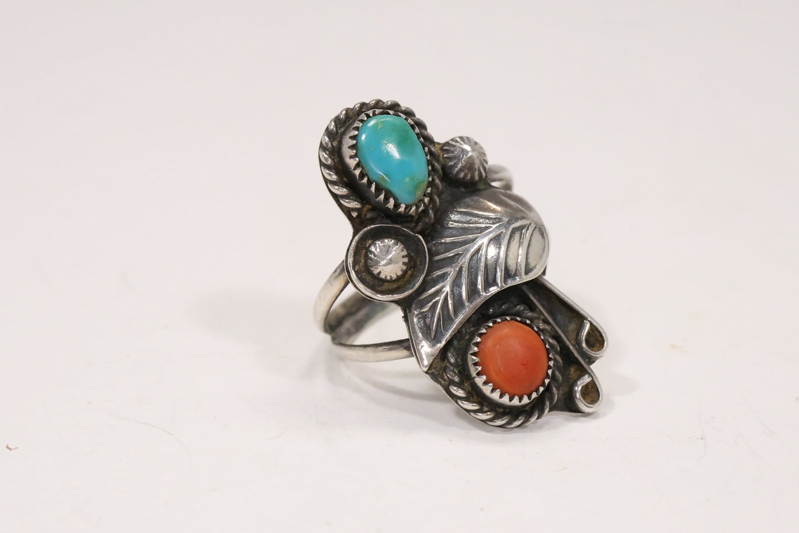 Navajo Style Sterling Turquoise and Coral Ring: A sterling silver ring has a rectangular setting with turquoise and coral cabochons surrounded by applied silver ornament. The materials and construction support a Navajo style description but no