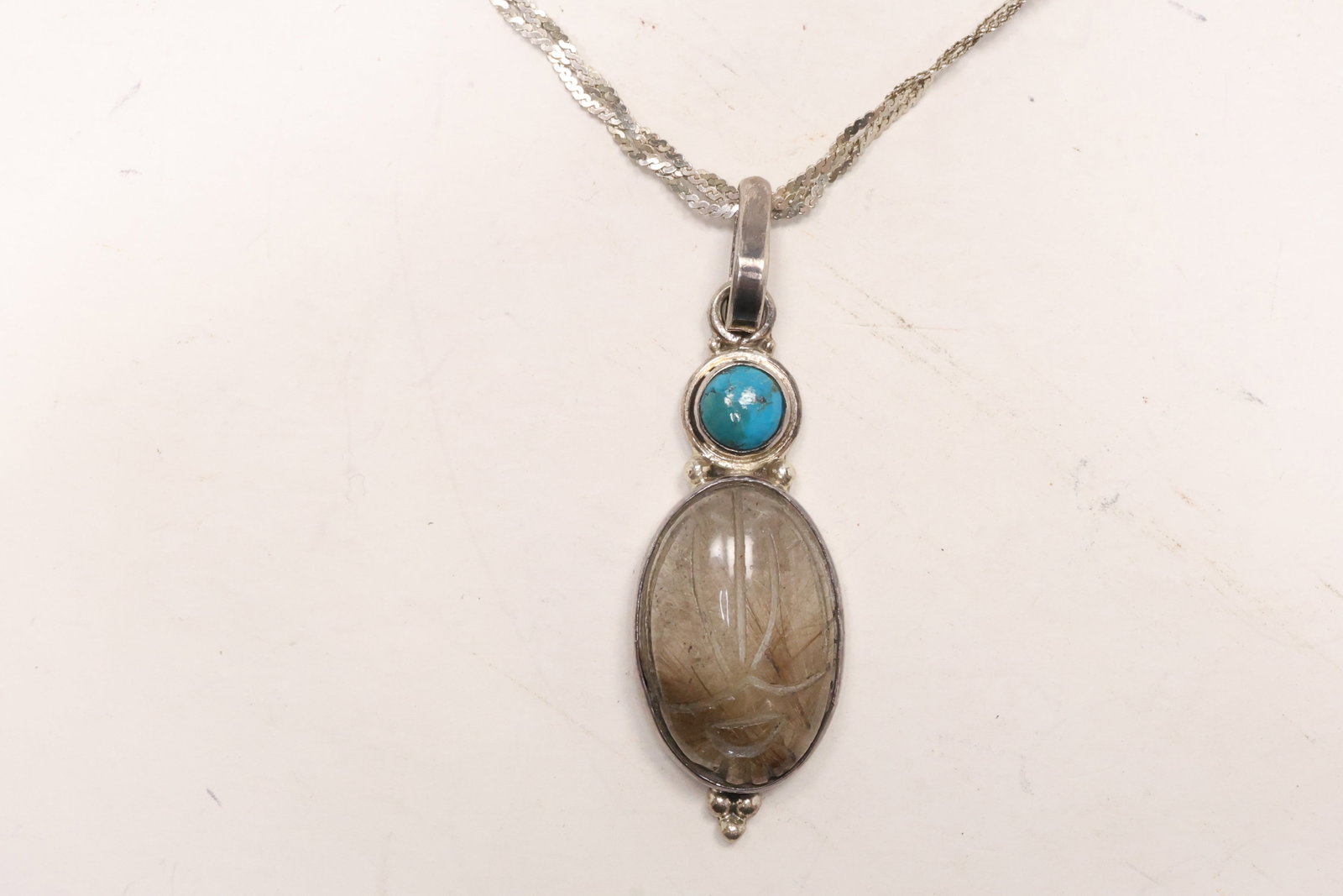 Sterling Silver Scarab Stone and Turquoise Pendant Necklace: A sterling silver pendant necklace combines an oval scarab carved stone with a turquoise cabochon on an Italy marked braided chain. The stacked gemstone and elongated pendant format are visible in