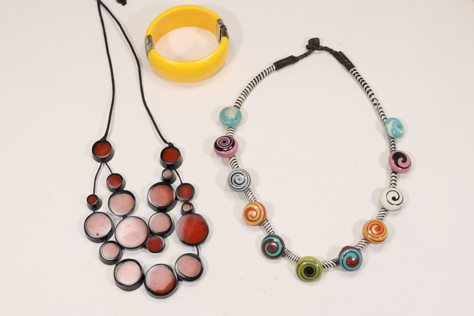 Three Modernist Disc and Rope Necklaces with Cuff Bracelet: A modernist costume jewelry group includes graduated red and black disc necklaces a hand made striped rope necklace with swirl buttons and a yellow cuff bracelet. The bold colors and oversized