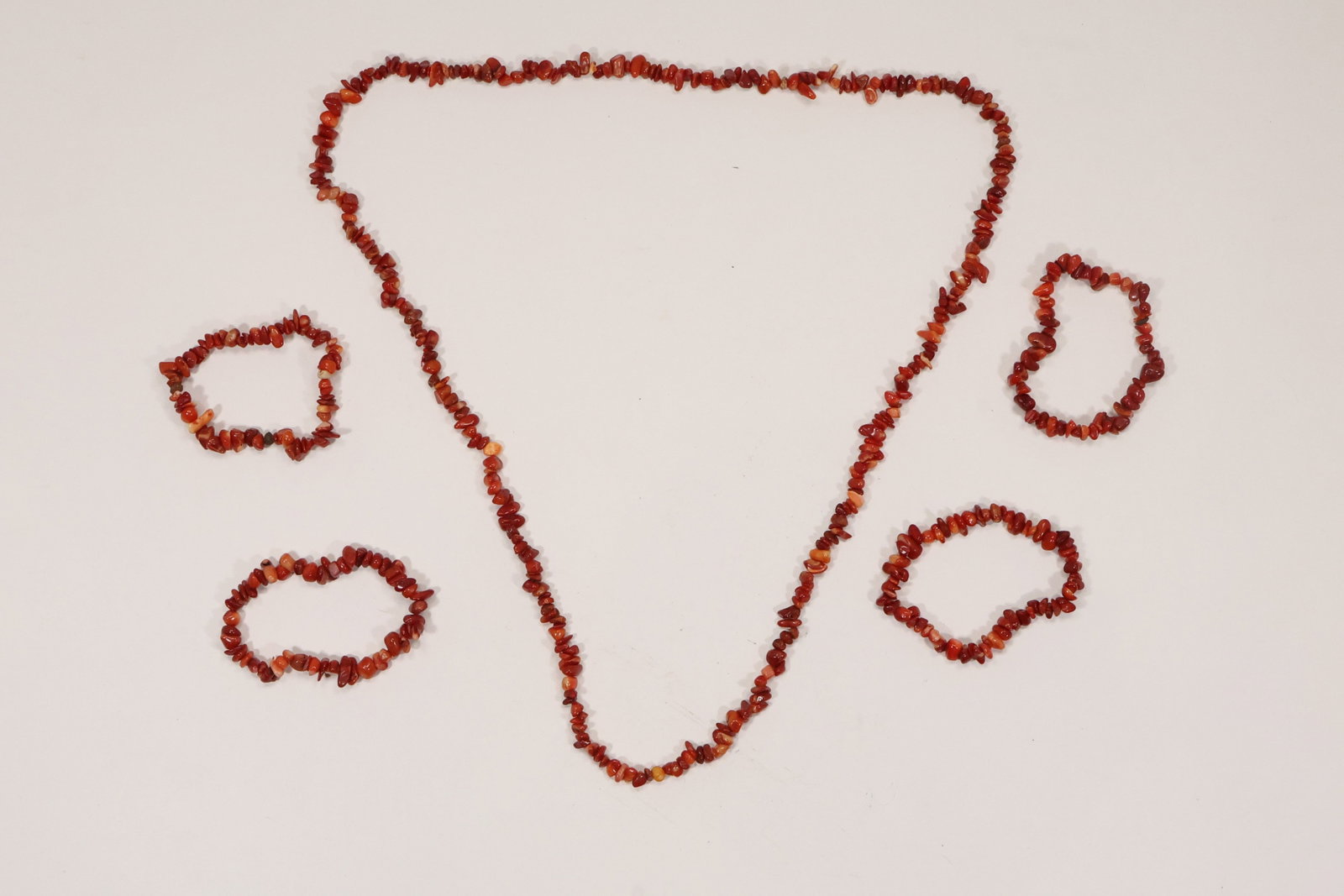 Coral Chip Necklace and Four Bracelet Group: A jewelry group includes one long coral chip necklace and four coordinating stretch or strand bracelets. The irregular branch and chip beads create a layered red orange organic texture. The