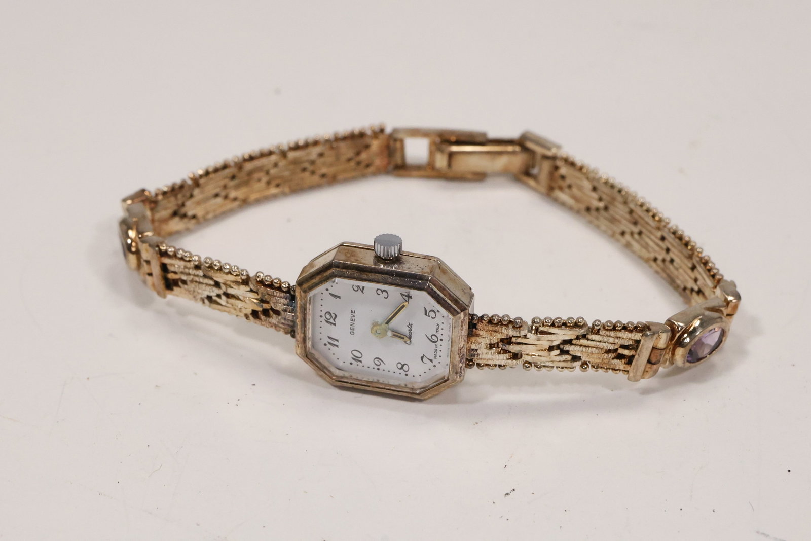Geneve Sterling Silver Amethyst Ladies Wristwatch: A ladies wristwatch has a Geneve signed dial and an Italy marked .925 sterling silver bracelet set with purple amethyst stones. The square watch case and decorative stone set links create a jewelry wa