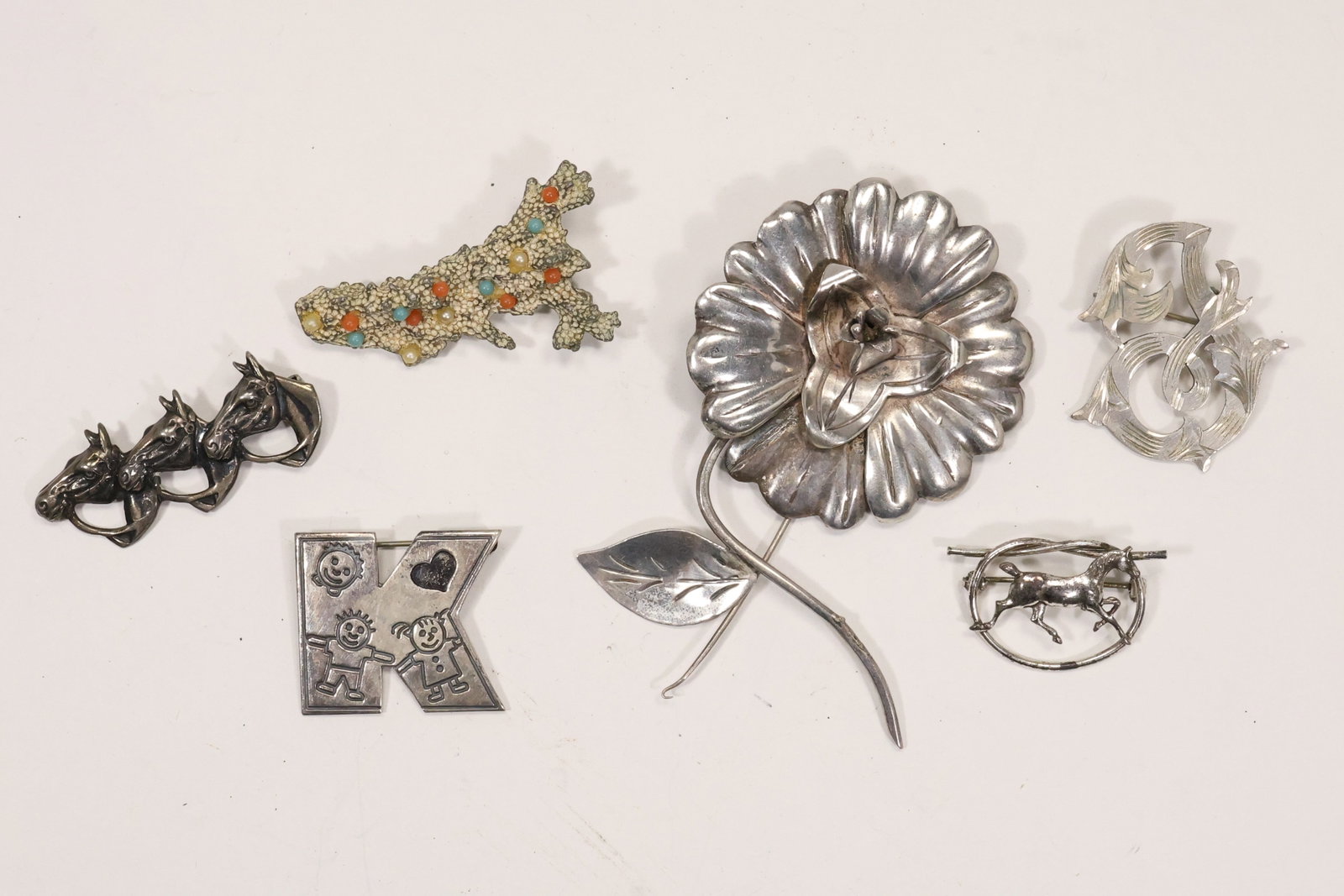 Sterling Silver Figural and Mexican Pin Collection: A sterling silver pin group includes coral reef flower letter K swirl horse triple horse head and other figural designs. Mexican marks and maker codes are retained in the original catalog notes where 