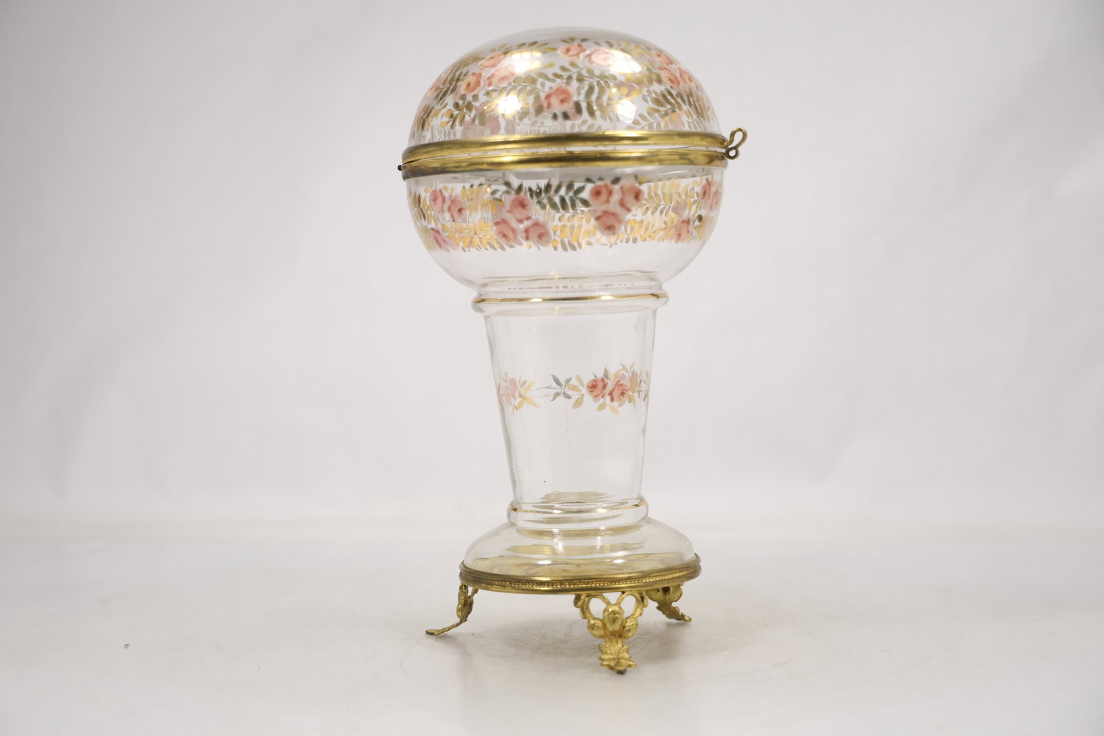 French Style Gilt Metal Mounted Enameled Glass Liquor Cave: A globe form liquor cave or tantalus has a clear glass body decorated with multicolor floral enamel and fitted with hinged gilt metal mounts finial and pedestal base. The opening spherical form and in
