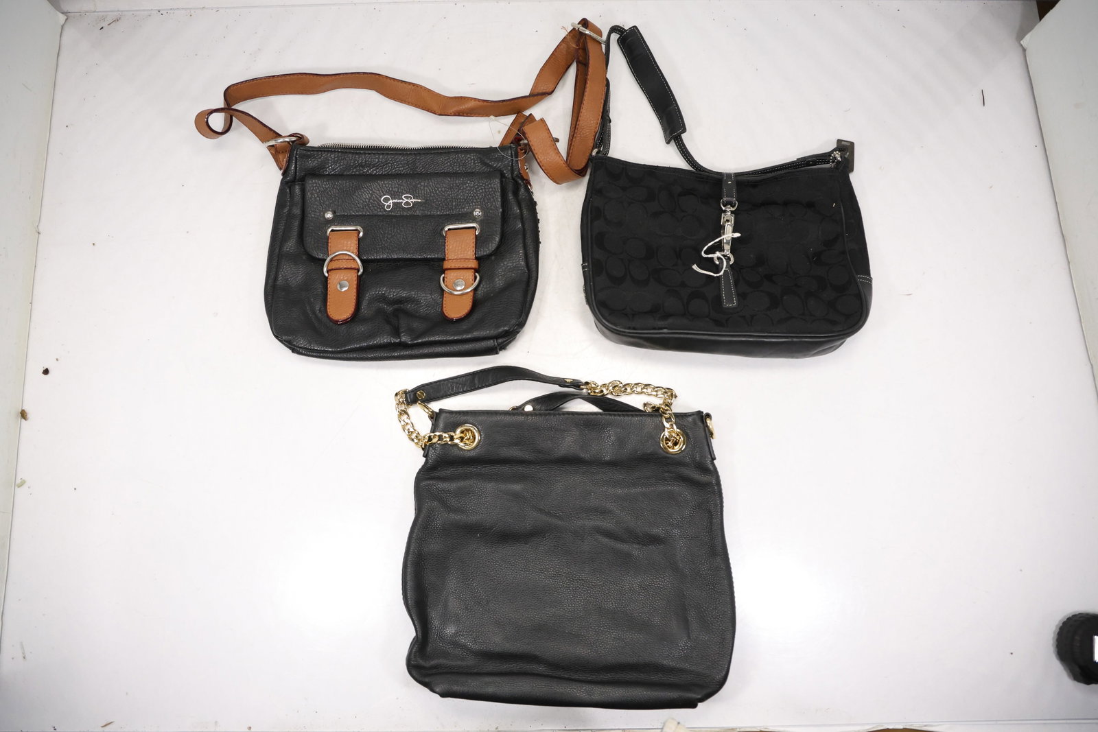 Three Black Leather and Fabric Shoulder Bags: A group of three black shoulder bags combines leather and textile bodies with tan trim flap closures and adjustable straps. The mixed day bag forms are presented without unsupported maker attributions