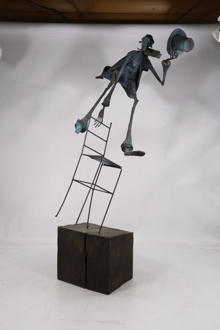 Large Figural Chair Trick Mechanical Novelty Sculpture: A large mechanical novelty sculpture depicts a human figure associated with a chair and articulated trick mechanism. The painted metal construction and theatrical action format are visible in the phot
