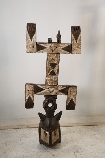 Large Carved Wood Warrior Tiki Wall Sculpture: A large carved wood wall sculpture has a horizontal architectural form with a central stylized warrior or tiki figure between geometric end panels. The incised surface and symmetrical composition supp