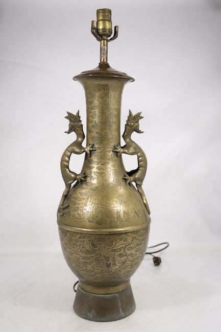 Asian Style Brass Dragon Handle Urn Table Lamp: A brass table lamp has an urn form body with paired dragon handles relief ornament flared neck and electrical fittings. The Asian inspired decorative vocabulary is visible in the cast metalwork and