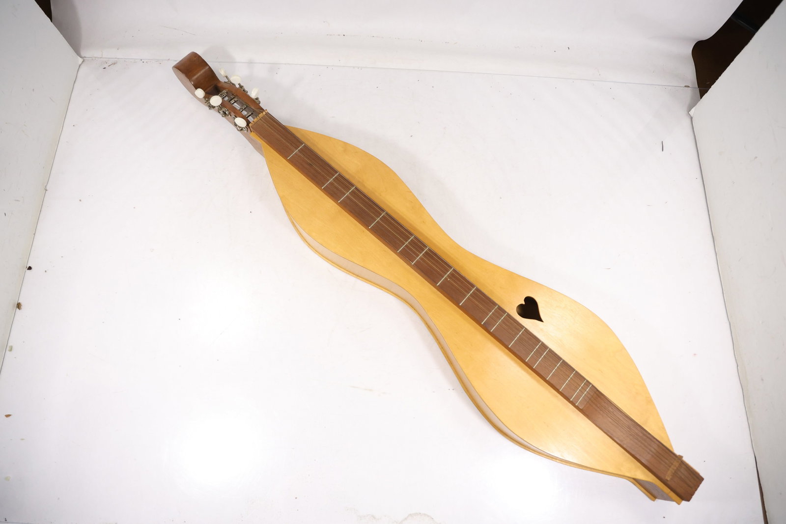 Unmarked Classical Acoustic Guitar: A full size acoustic guitar has a natural wood body slotted headstock six strings and a dark bridge. No legible maker name or model mark is confirmed in the photographs. The acoustic instrument form