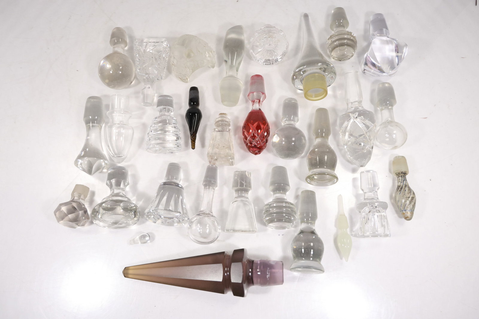 Collection of Twenty Nine Assorted Glass Stoppers: A collection contains approximately twenty nine assorted glass bottle and decanter stoppers in clear colored cut molded and faceted forms. The mixed group is suited to restoration replacement or