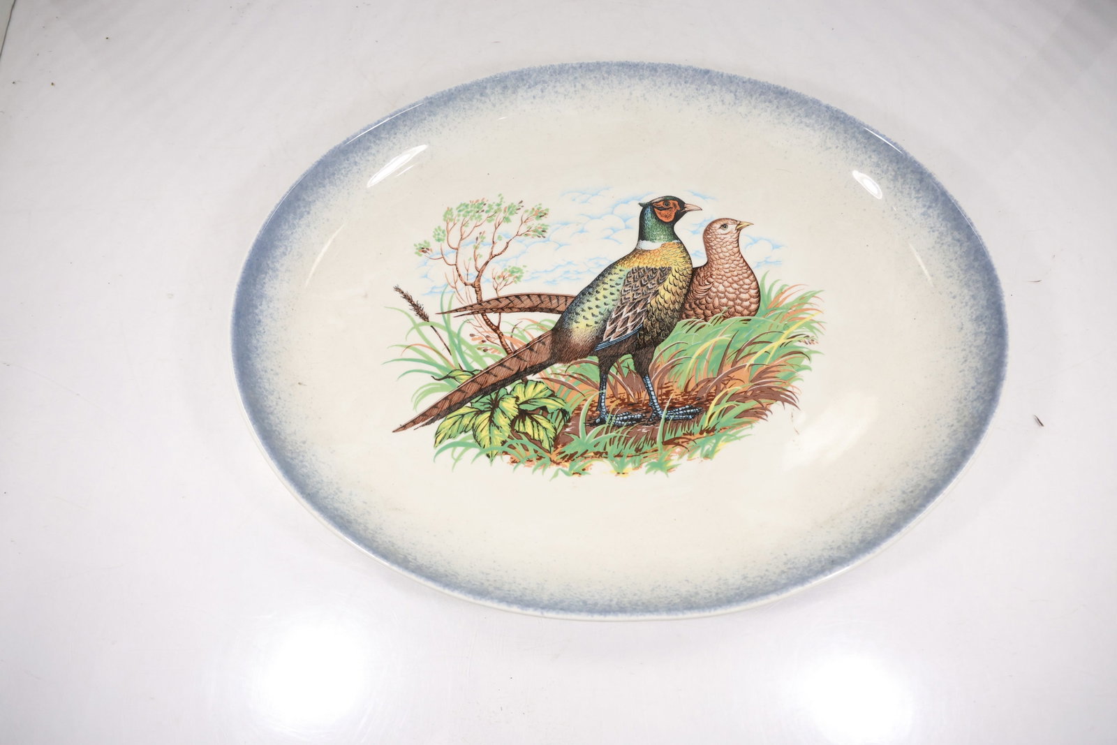 Pheasant Decorated Ceramic Platter on Silverplate Stand: A wide oval ceramic platter depicts pheasants in a landscape and rests in a fitted silverplate pedestal stand with decorative supports. The ceramic image and metal serving mount form a combined