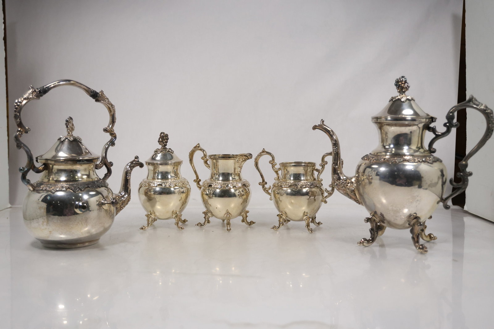 Five Piece Silverplate Tea and Coffee Service: A coordinated five piece silverplate service includes a teapot coffee pot creamer sugar bowl and serving tray or waste bowl. The matching bodies curved handles and formal table service profiles