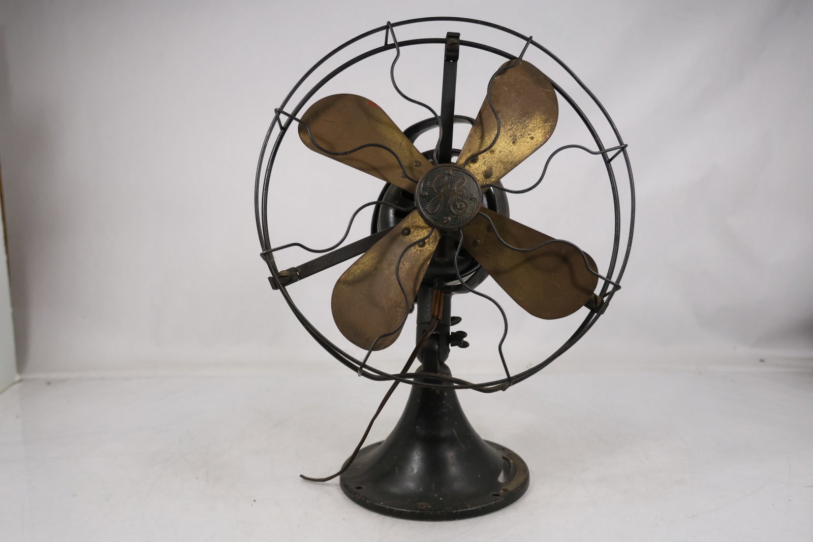 Vintage Electric Desk Fan with Brass Blades: Vintage electric desk fan with brass tone blades circular wire guard dark metal motor housing and weighted base. The compact industrial form combines functional machinery with decorative early