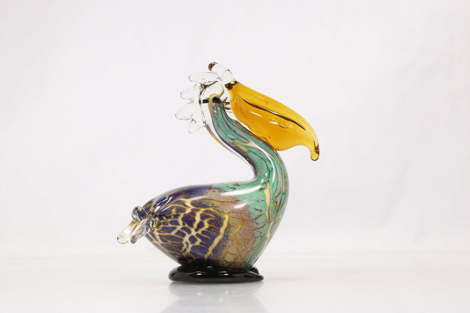 Colorful Hand Blown Art Glass Pelican Sculpture: Hand blown art glass pelican with clear body yellow beak and green amber and blue applied color details. The sculptural bird form uses pulled glass elements for the wings tail and bill. The form relat