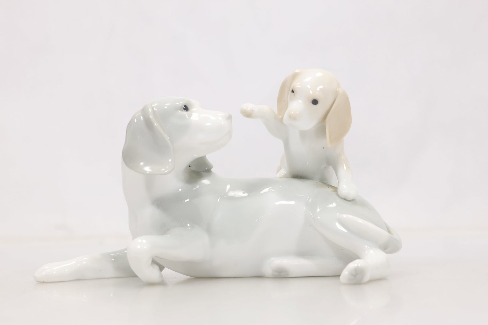 Playful Moment Porcelain Dog Figurine: Glazed white porcelain sculpture of two playful dogs with softly modeled forms and pale painted accents. The underside mark identifies Playful Moment with a printed maker inscription. The modeling