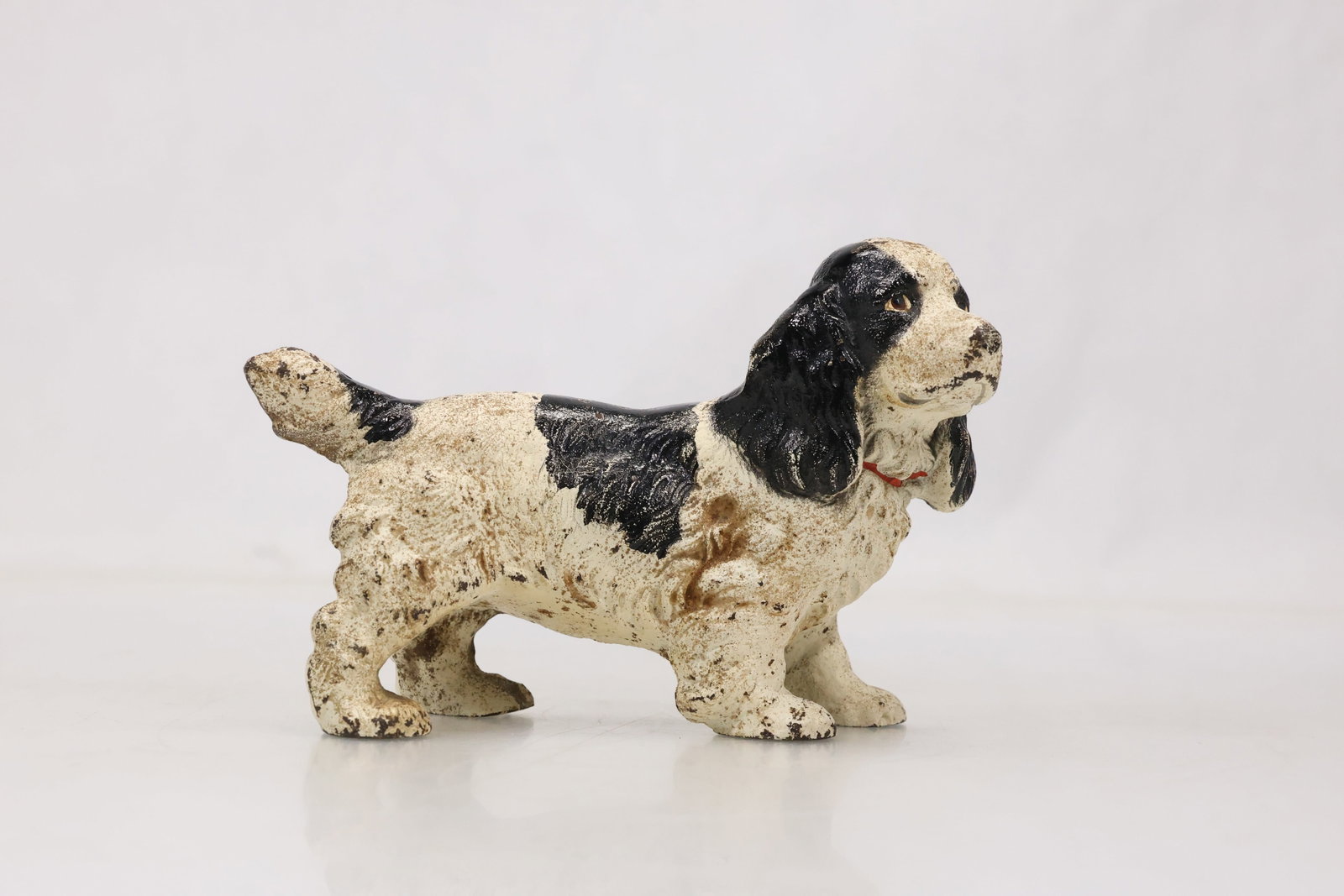 Painted Ceramic Long Haired Dog Figurine: Modeled ceramic dog figure with long textured coat dark ears and painted facial details. The low horizontal pose emphasizes the animals flowing fur and alert expression. The modeling relates to Europe