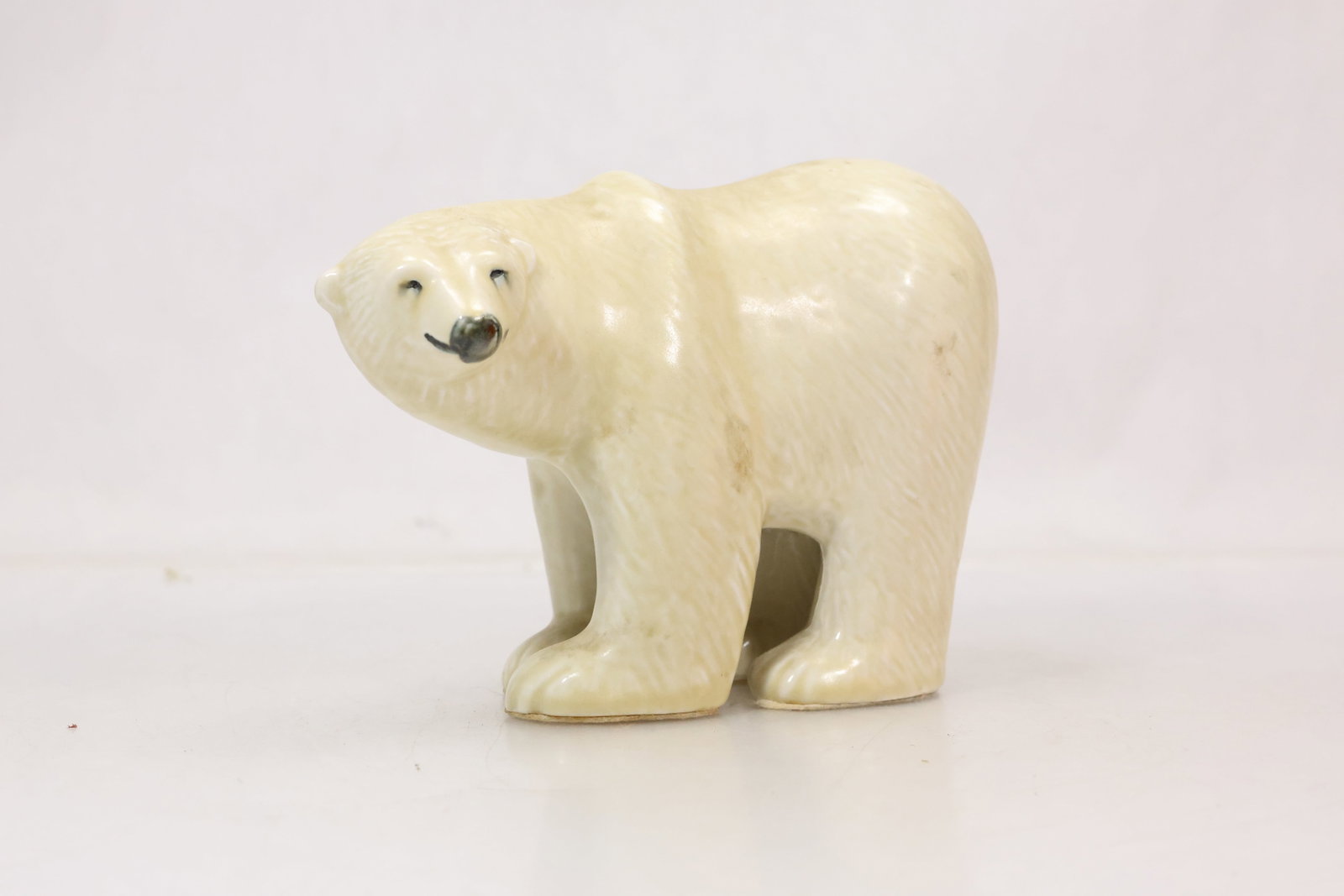 Glazed Ceramic Polar Bear Sculpture: Cream glazed ceramic polar bear figure modeled in a standing pose with rounded body dark eyes and black nose. The restrained palette emphasizes the sculptural silhouette and animal form. The form