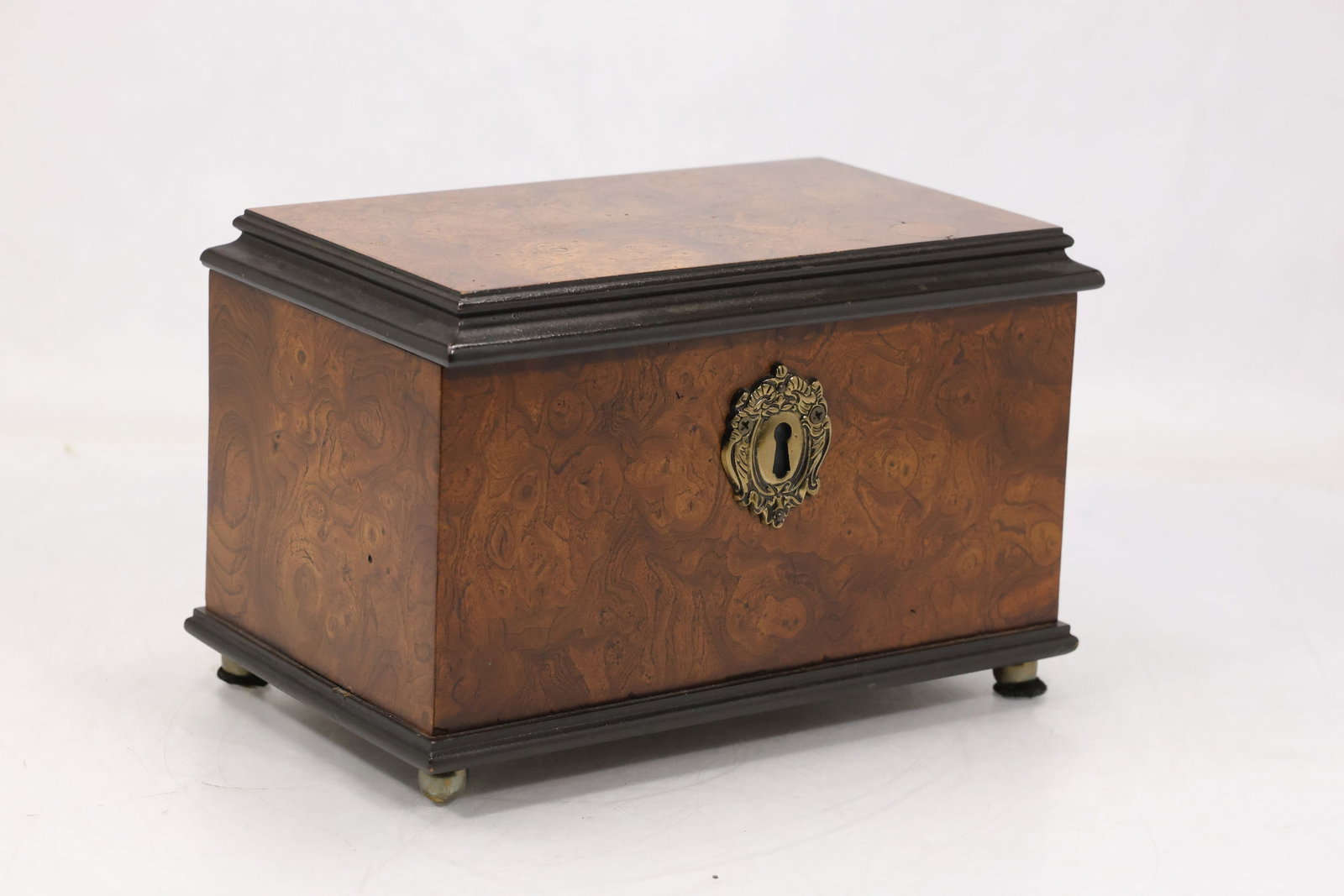 Decorative Wood Chest with Brass Hardware: Rectangular wood chest with hinged lid brass tone lock plate corner details and shaped metal pulls. The compact case displays warm grain and traditional campaign style hardware. The design relates to 