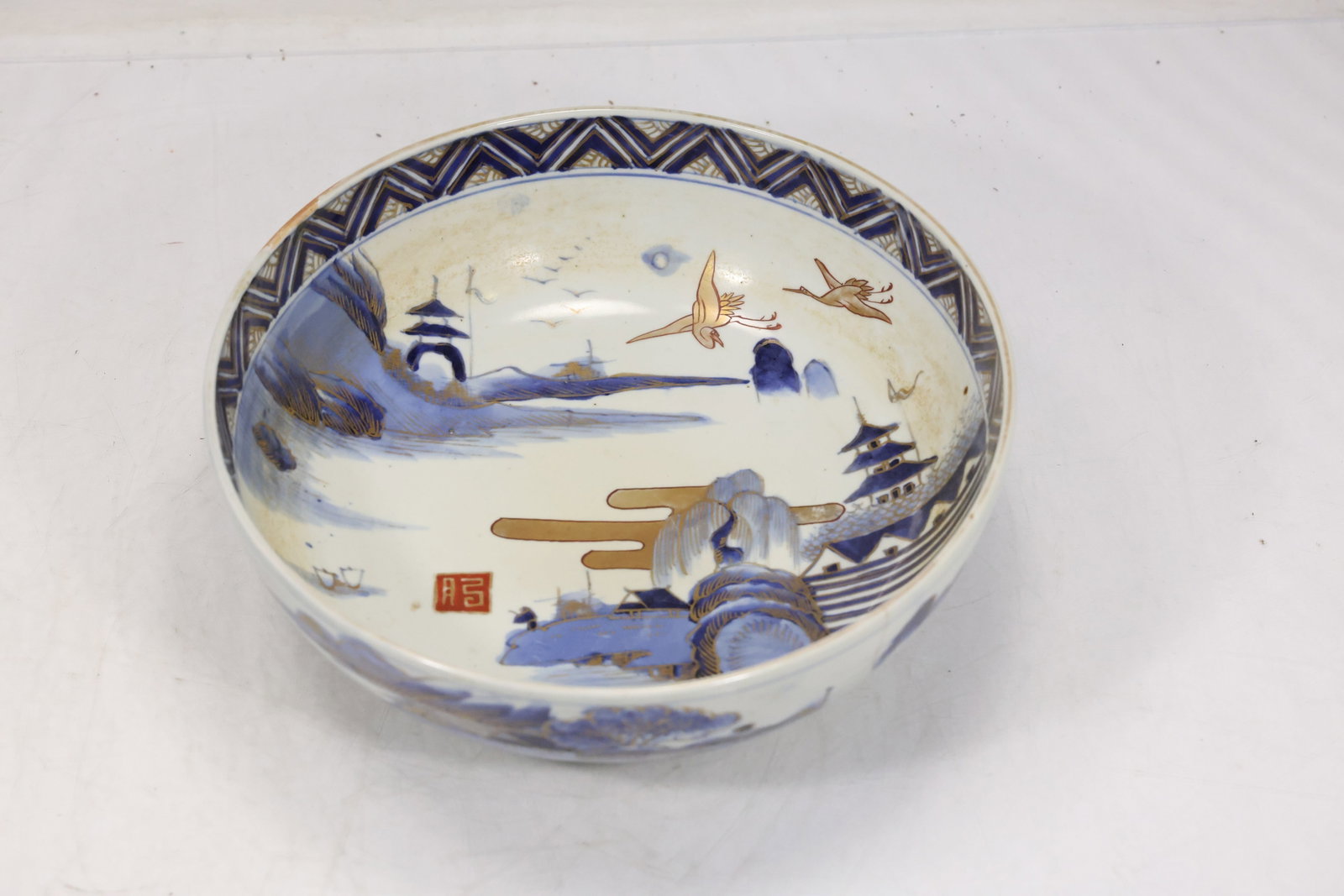 Chinese Blue and White Landscape Bowl: Chinese style porcelain bowl painted in underglaze blue with landscape architecture and floral border decoration. The deep rounded body and repeating rim pattern follow traditional export porcelain