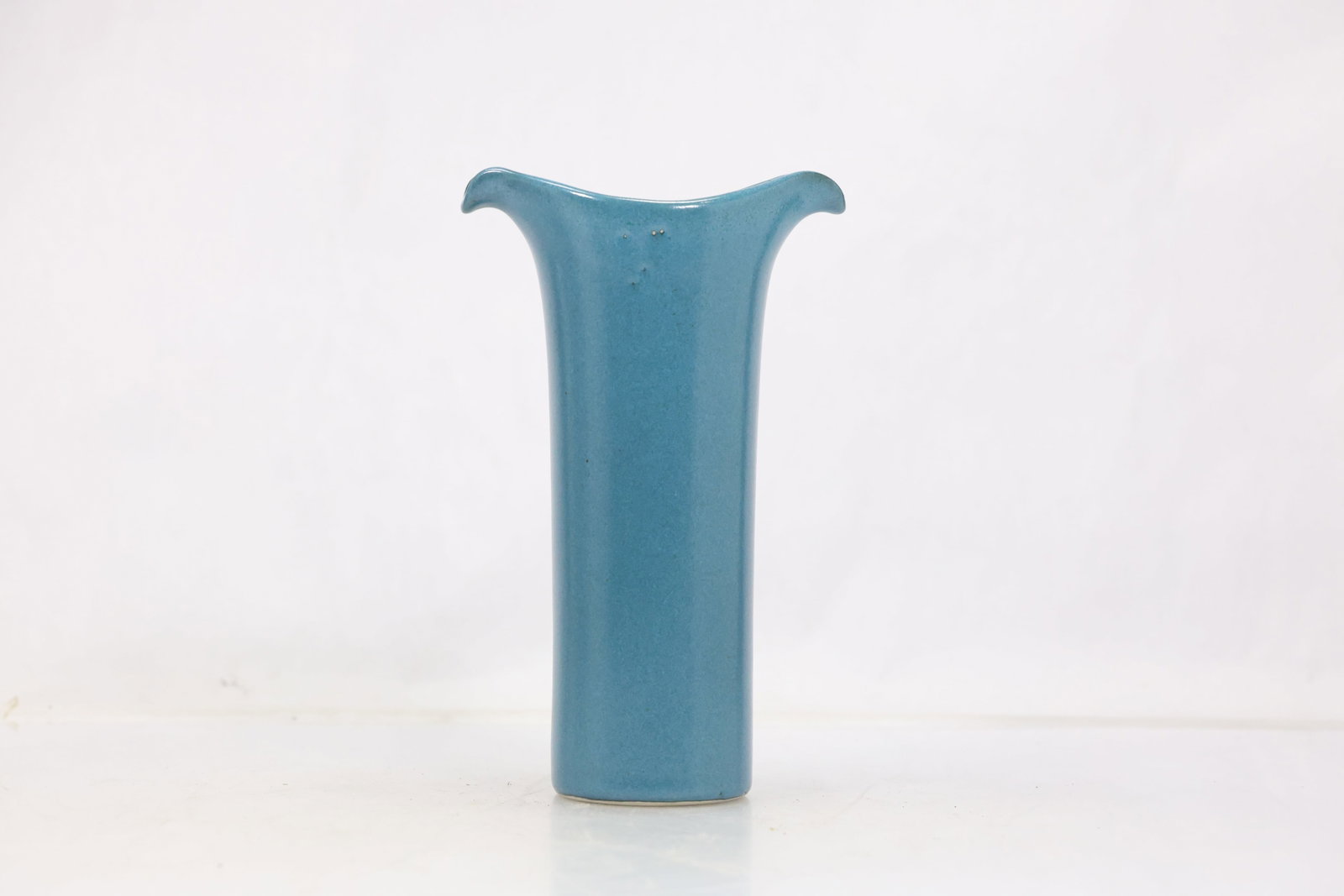 Blue Opaline Art Glass Bud Vase: Tall slender blue glass bud vase with narrow cylindrical neck flared rim and gently rounded body. The opaque color and clean silhouette emphasize a modern decorative form. The form relates to