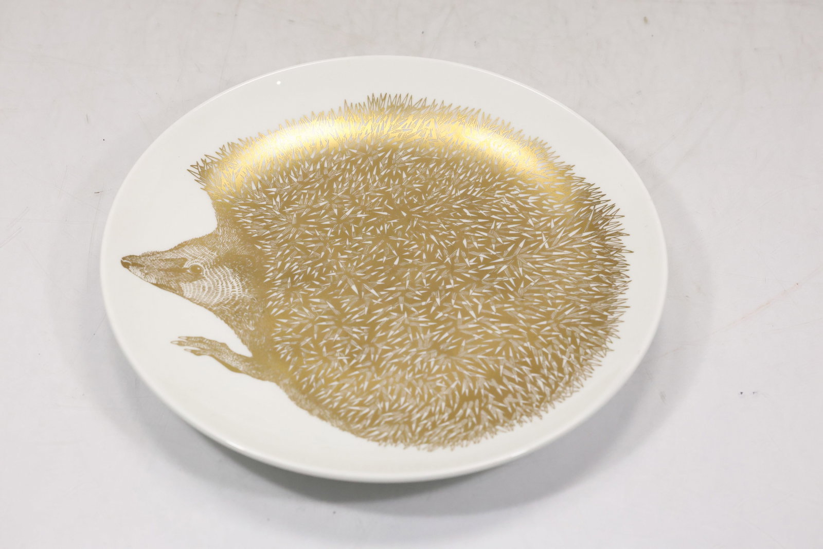 Textured Porcupine Motif Art Plate: Decorative round art plate with a raised porcupine or radiating quill motif across a pale textured surface. A printed artists card accompanies the sculptural plate in the photographs. The subject