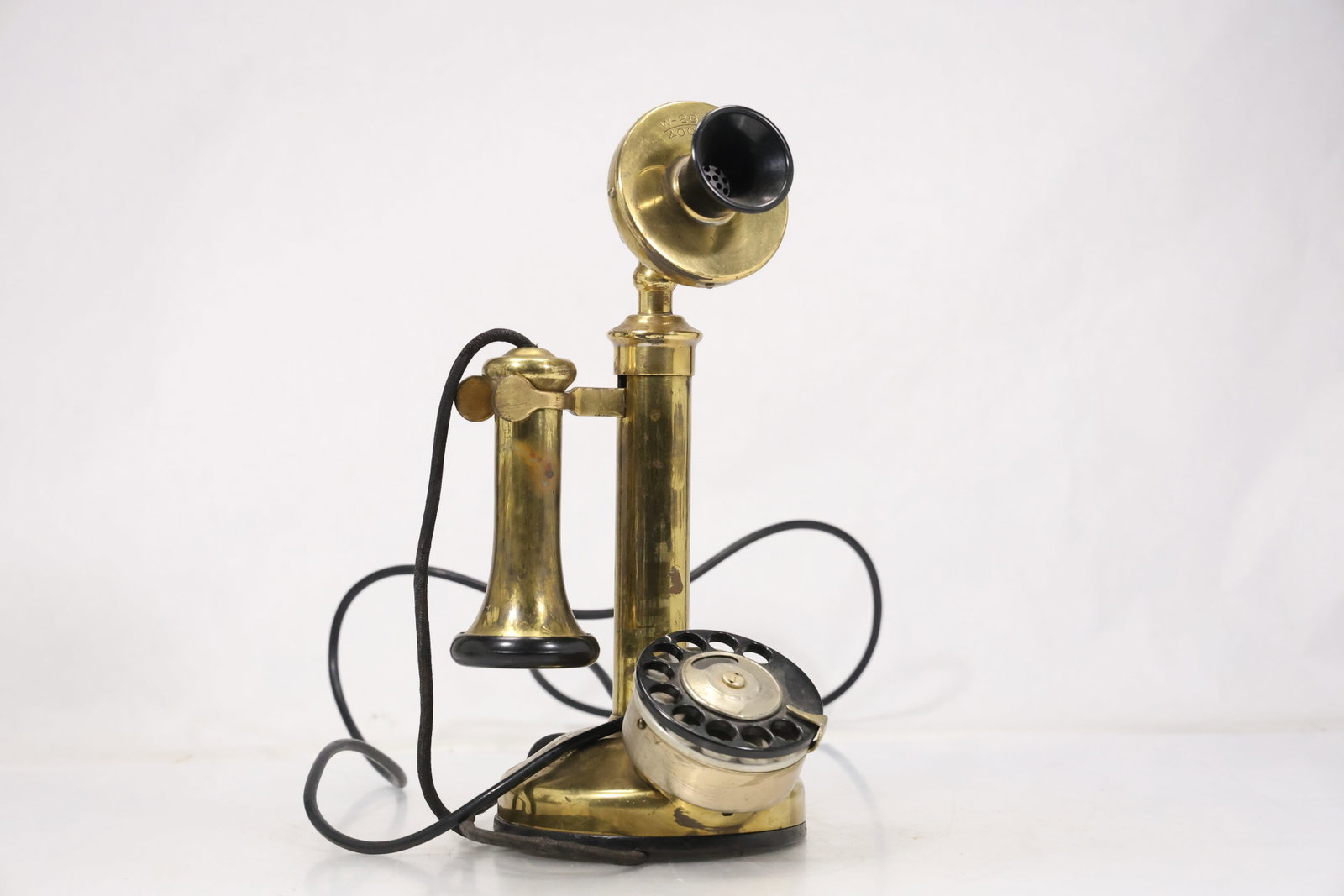 Vintage Style Brass Candlestick Telephone: Decorative candlestick telephone with brass tone upright receiver support rotary dial handset and black cord. The design recreates early twentieth century telephone forms for display or use. The desig
