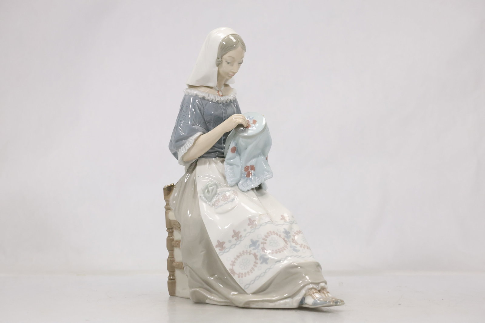 Marked European Porcelain Lady Figurine: Glazed porcelain figure of a seated woman in period dress with hand painted pastel and gilt details. A blue printed crown and maker mark appear on the underside. The modeling relates to European