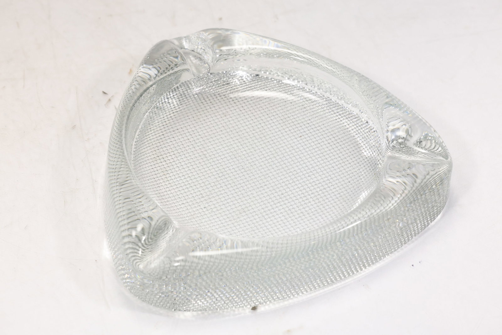 Clear Art Glass Freeform Ashtray: Heavy clear art glass ashtray with asymmetrical triangular form rounded corners and shaped cigarette rests. The thick polished glass creates a sculptural tabletop accessory. The form relates to