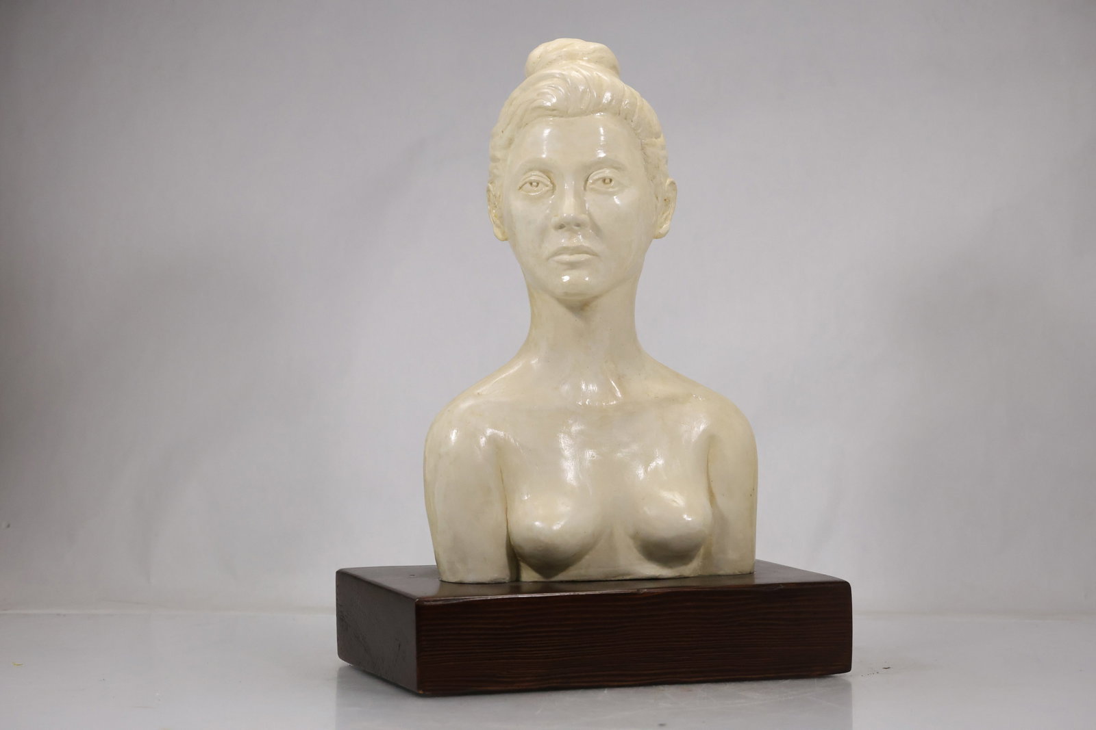 Classical Female Portrait Bust on Wood Base: Large cream colored portrait bust of a woman with softly modeled facial features coiffed hair and classical drapery mounted on a dark wood plinth. The frontal presentation emphasizes academic sculptur