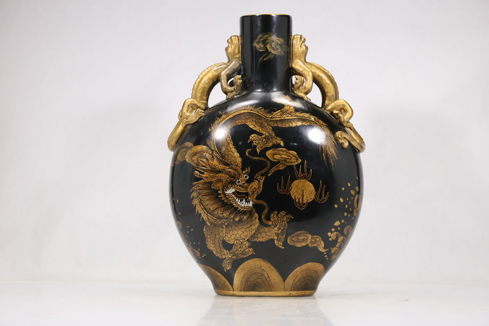 Large Black and Gold Dragon Porcelain Vase: Large black porcelain vase with rounded body narrow neck and extensive gold dragon cloud and botanical decoration. The high contrast palette and scrolling motifs create an East Asian inspired