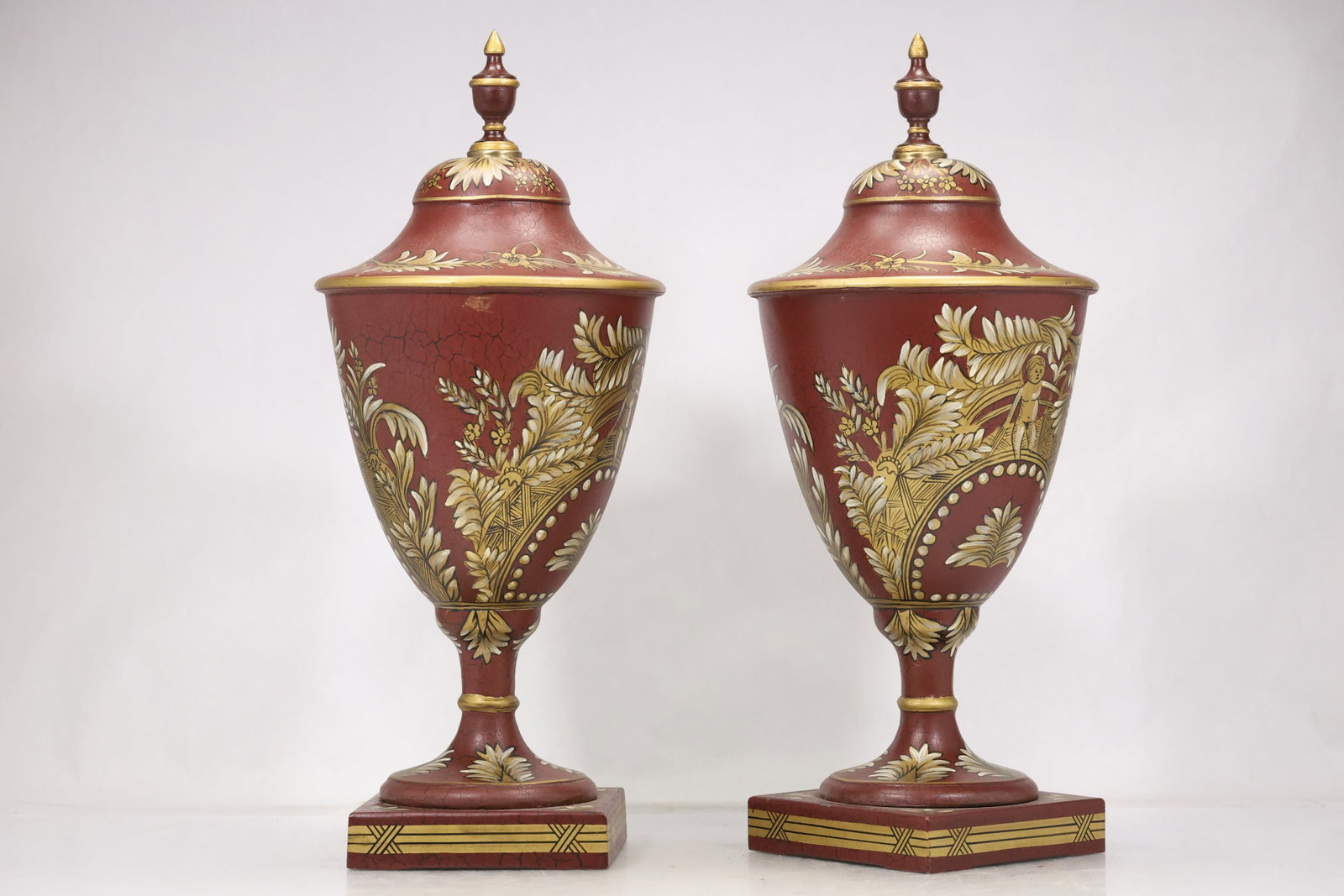 Pair Crackle Glaze Urn Form Vases: Pair of tall urn form vases with red crackle style grounds gilt botanical decoration domed covers and finial tops. Matching ornamental bands and classical profiles create a symmetrical display pair. T