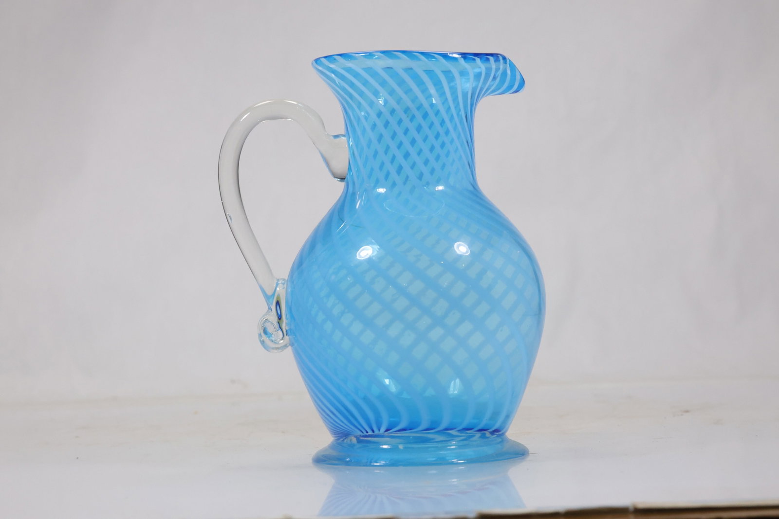 Blue Cased Art Glass Ewer Vase: Bright blue cased art glass ewer with ribbed body narrow neck flared rim and clear applied handle. The vivid opaque color and elongated pouring form create a modern decorative vessel. The form