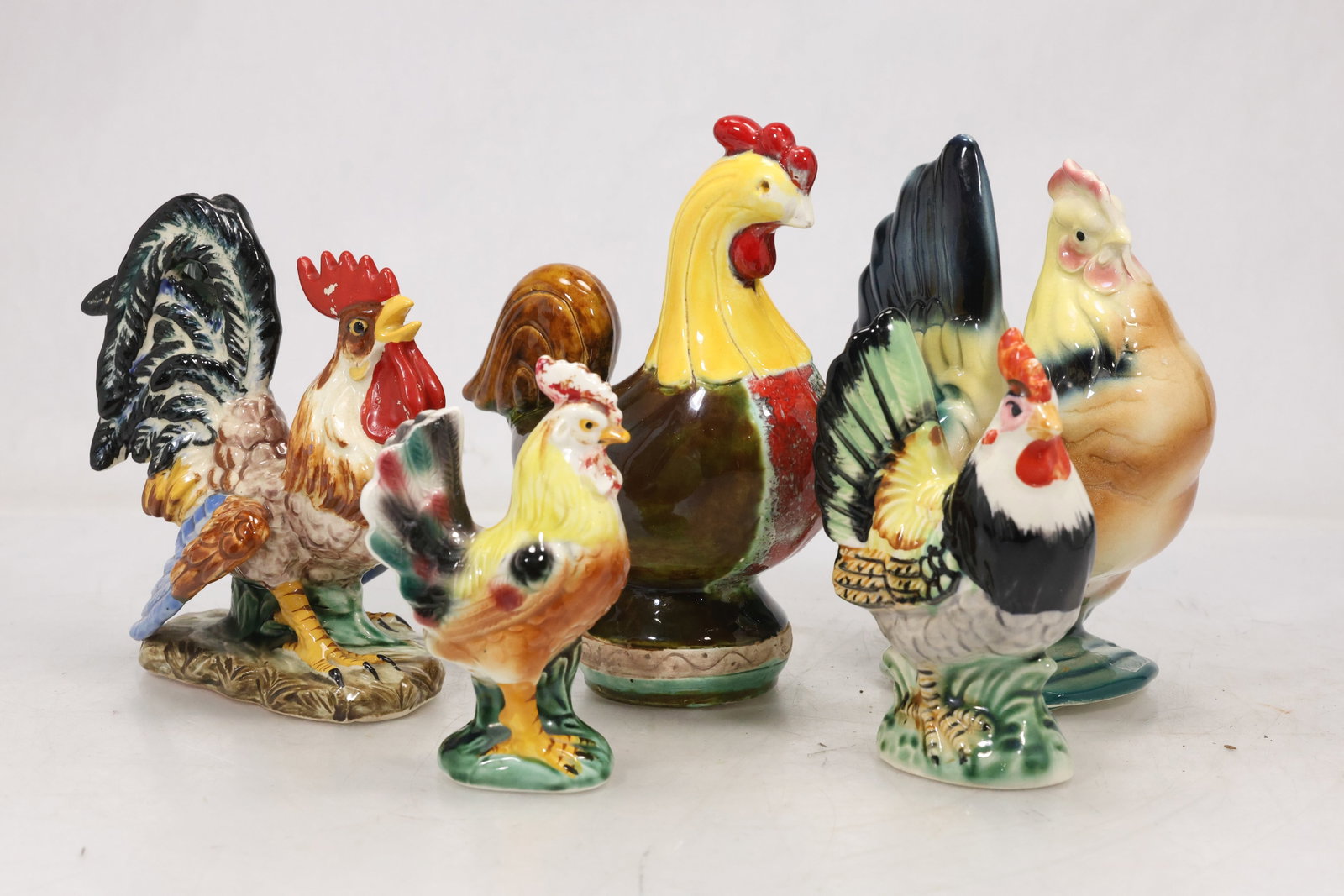 Group of Five Painted Ceramic Rooster Figures: Group of five ceramic rooster and chicken figures in varied sizes with colorful painted plumage. The modeled birds combine black white red yellow and green details for decorative display. The subject