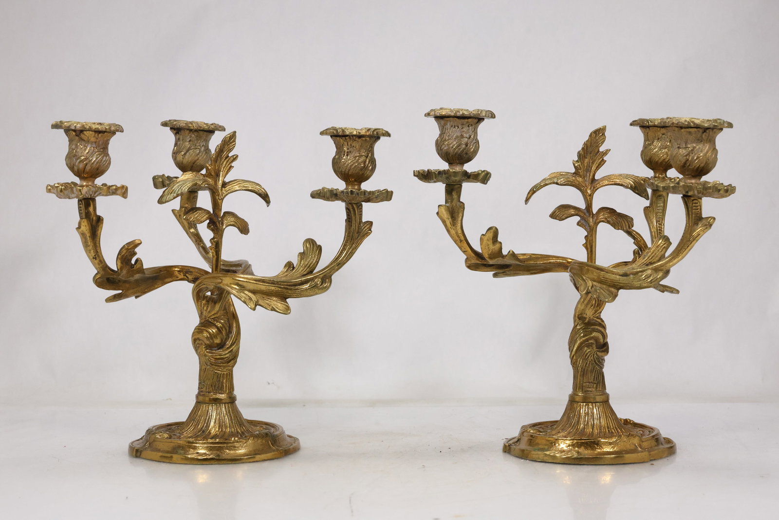 Pair Ornate Brass Five Light Candelabra: Pair of brass candelabra each with five scrolling candle arms foliate details and stepped central stems. The symmetrical revival style forms create a substantial mantel or dining table pair. The