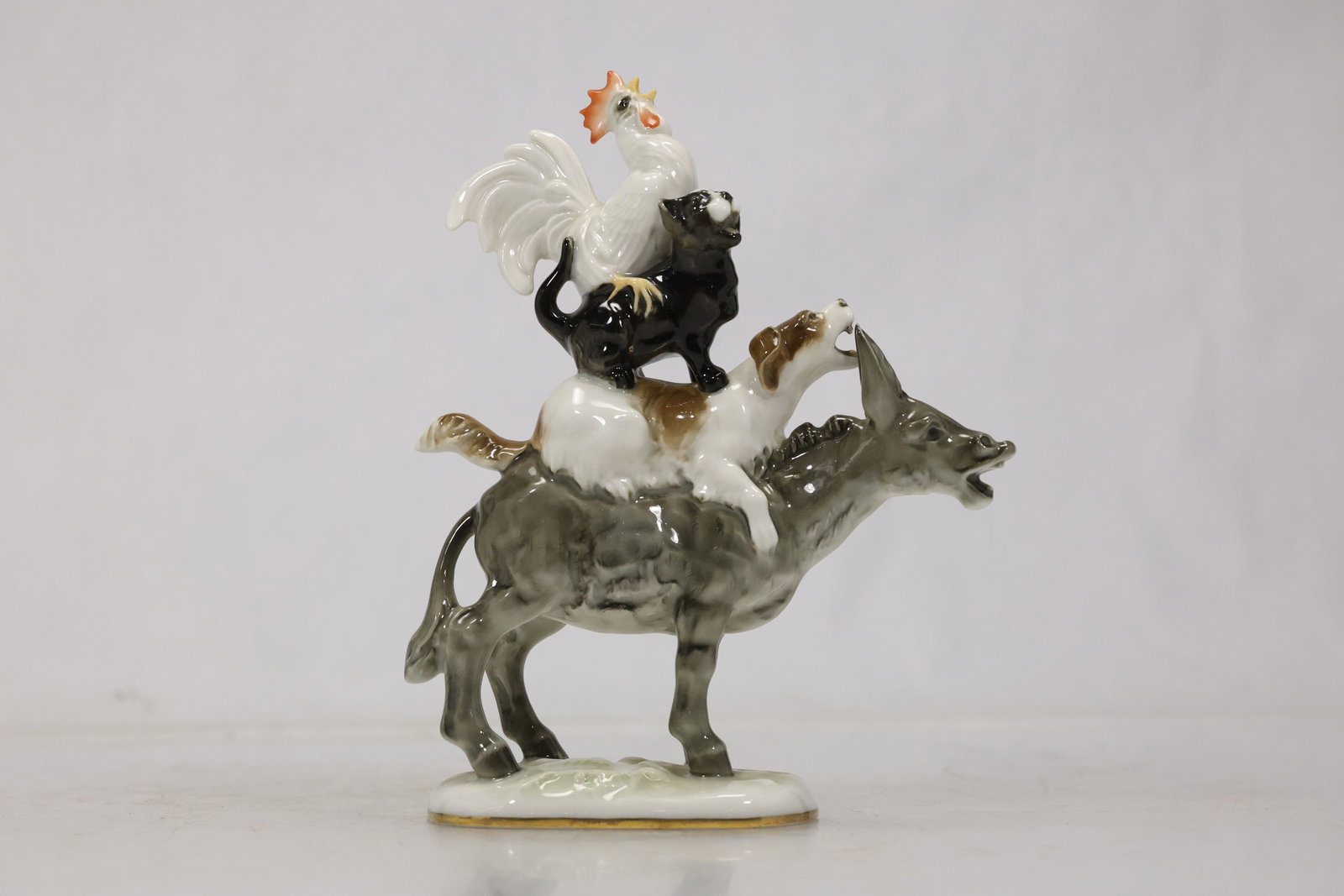 Schaubach Kunst Bremen Town Musicians Porcelain Figurine: Glazed porcelain sculpture depicting the Bremen Town Musicians with a donkey dog cat and rooster stacked in a vertical composition. The gray black white and orange painted details are accompanied by a